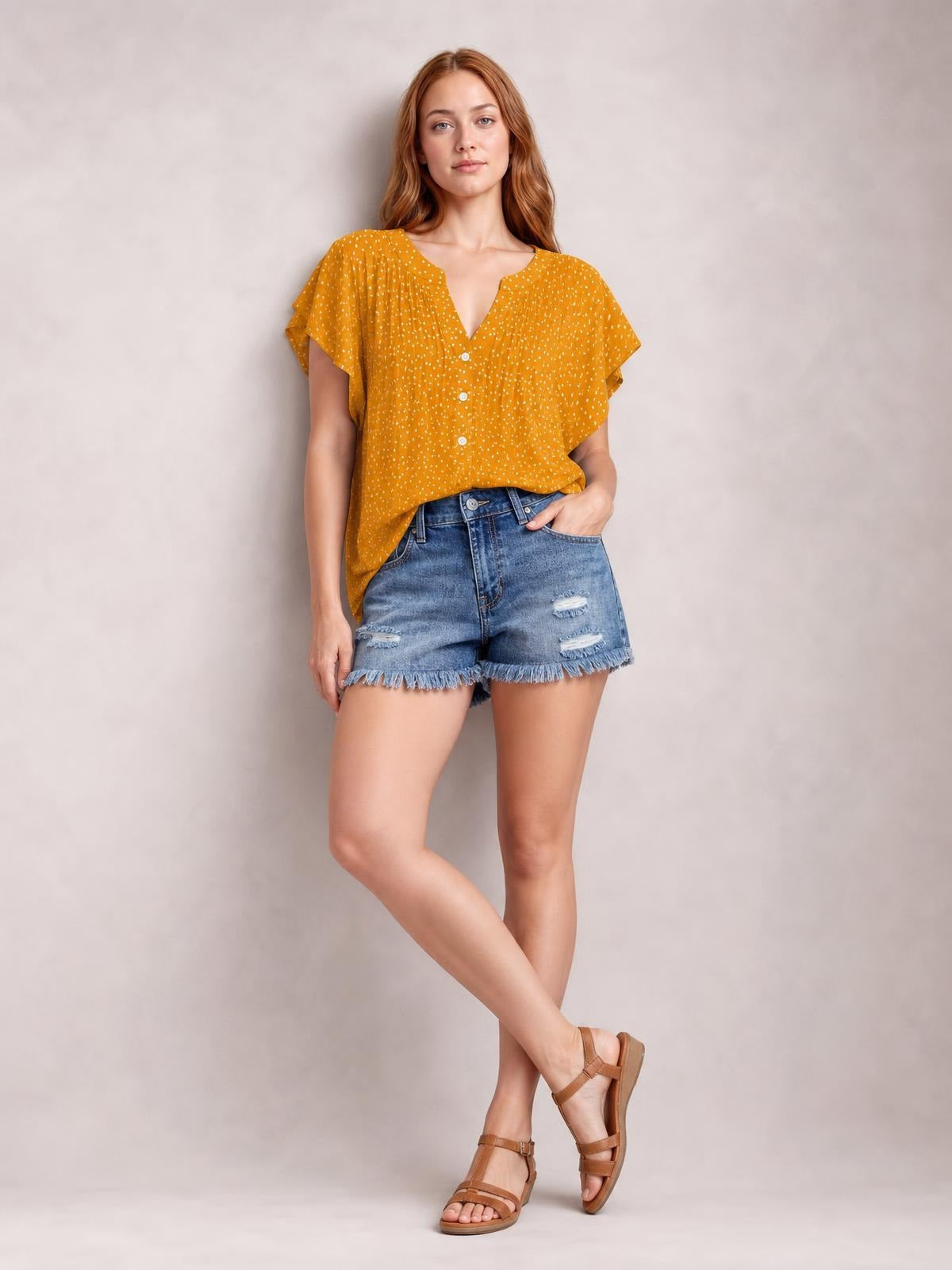 Model in a mustard polka dot blouse with a notched neckline, ruched front, ruffled cap sleeves, button placket, and relaxed silhouette.
