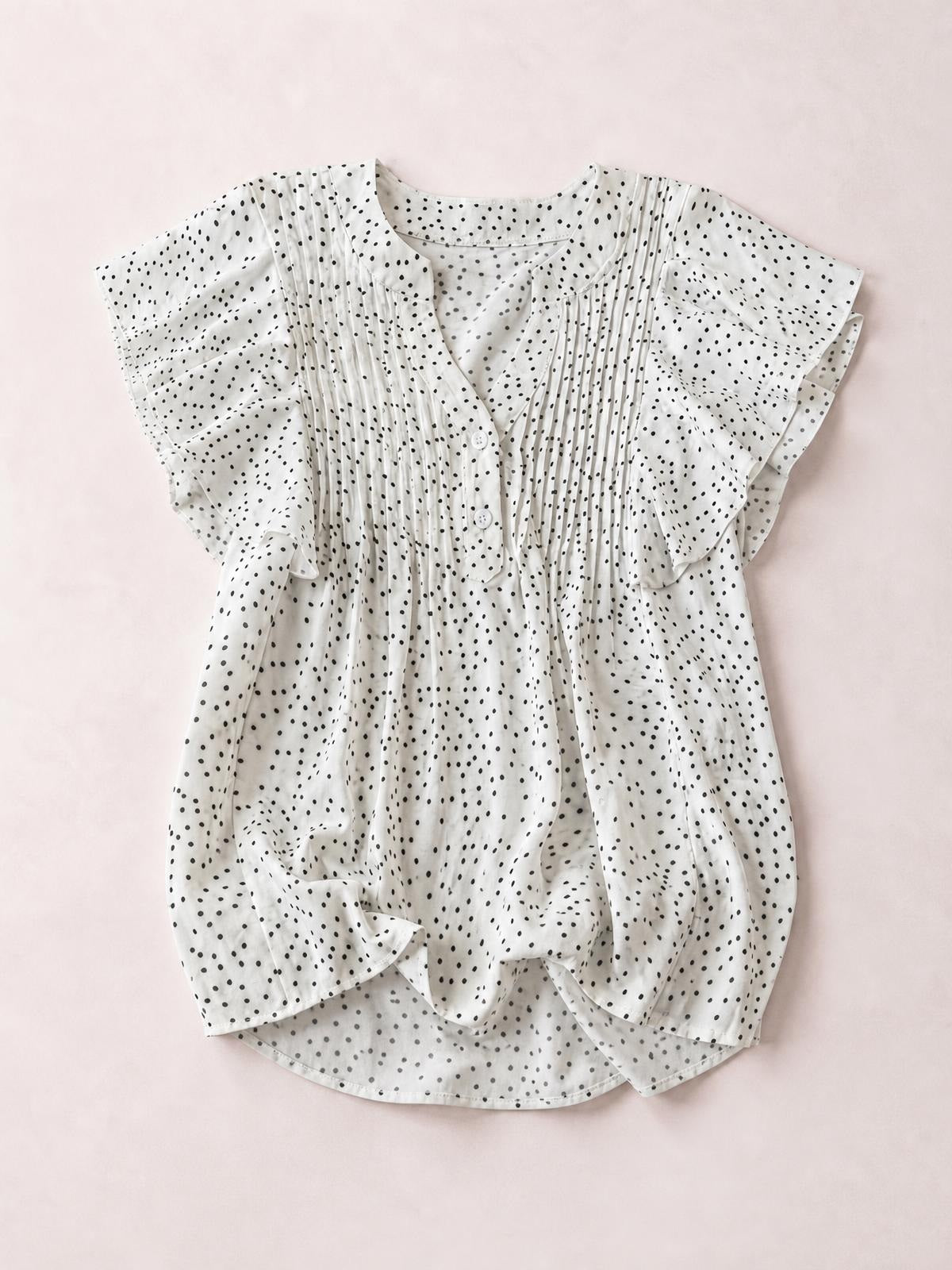 White polka dot blouse with a notched neckline, ruffled cap sleeves, ruched pleated front, button closure, and a relaxed silhouette.
