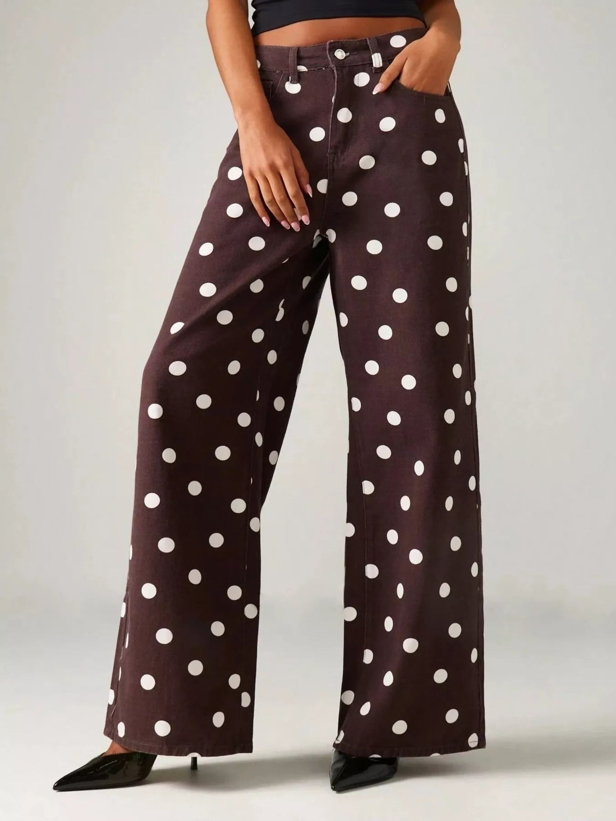 Model poses in dark brown polka dot wide-leg jeans with a high-rise button closure, side pockets, and relaxed full-length legs.