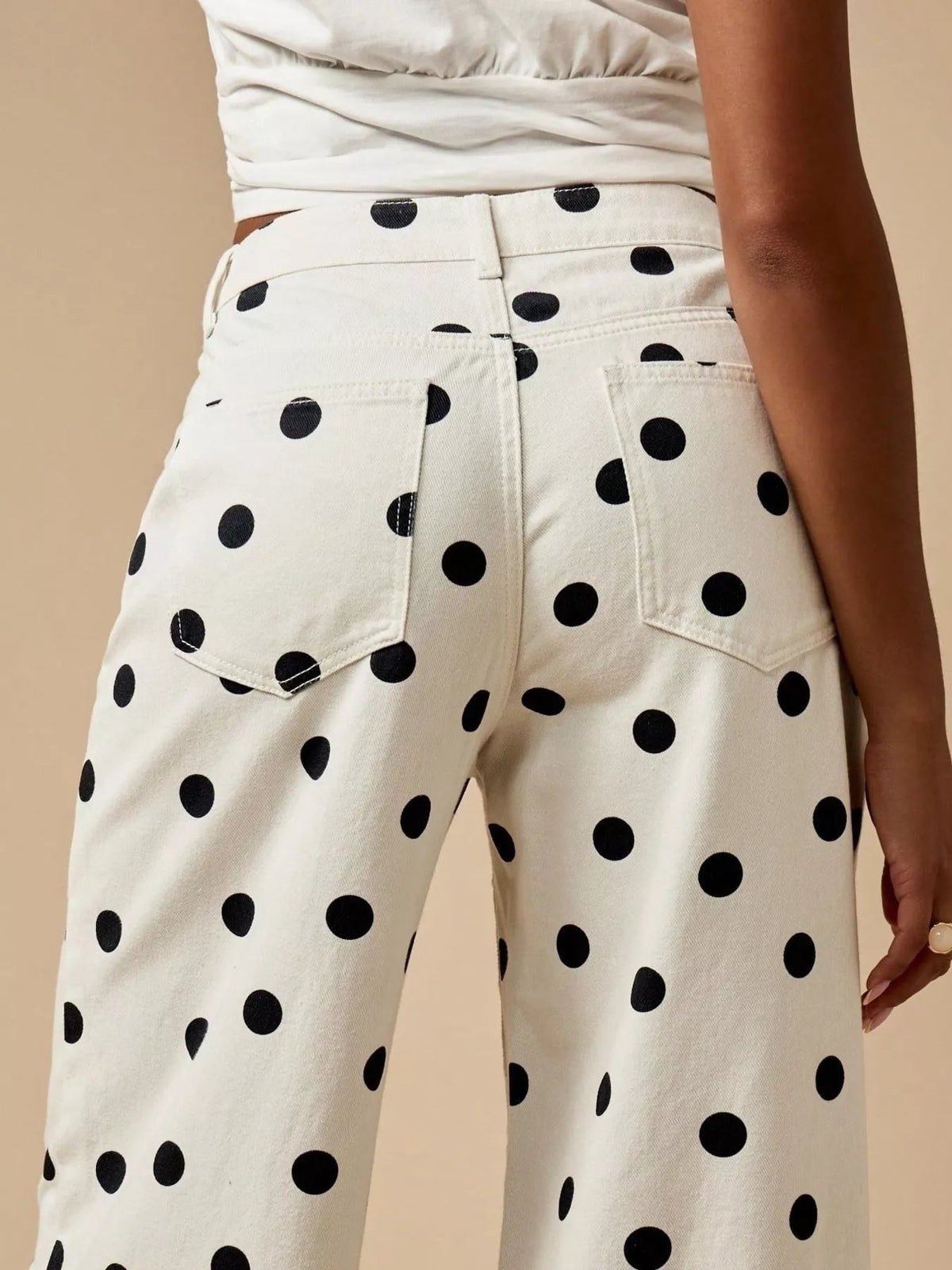 Model wears white polka dot wide-leg jeans with black spots, belt loops, button closure, and large back pockets, shown from behind.