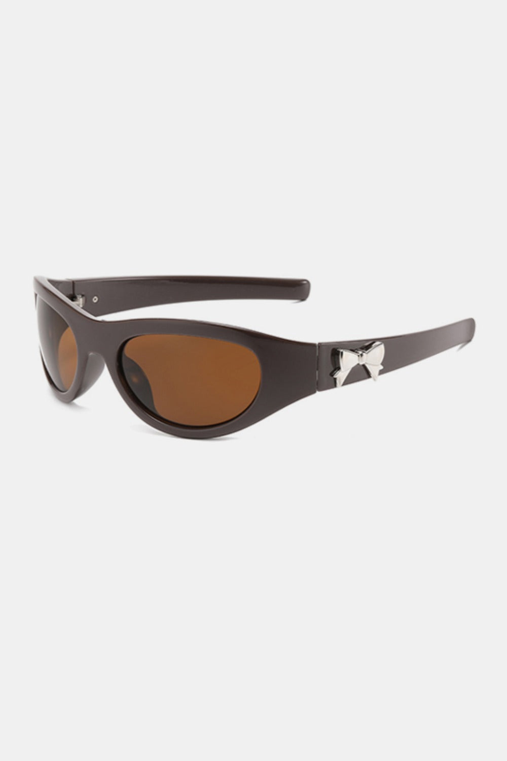Dark brown polycarbonate cat-eye sunglasses feature rounded amber lenses, softly upswept corners, tapered temples, and a subtle silver bow side detail.