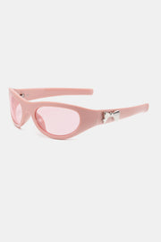 Pink polycarbonate cat-eye sunglasses feature rounded lenses, softly upswept corners, sleek tapered temples, and a silver bow-shaped side detail.