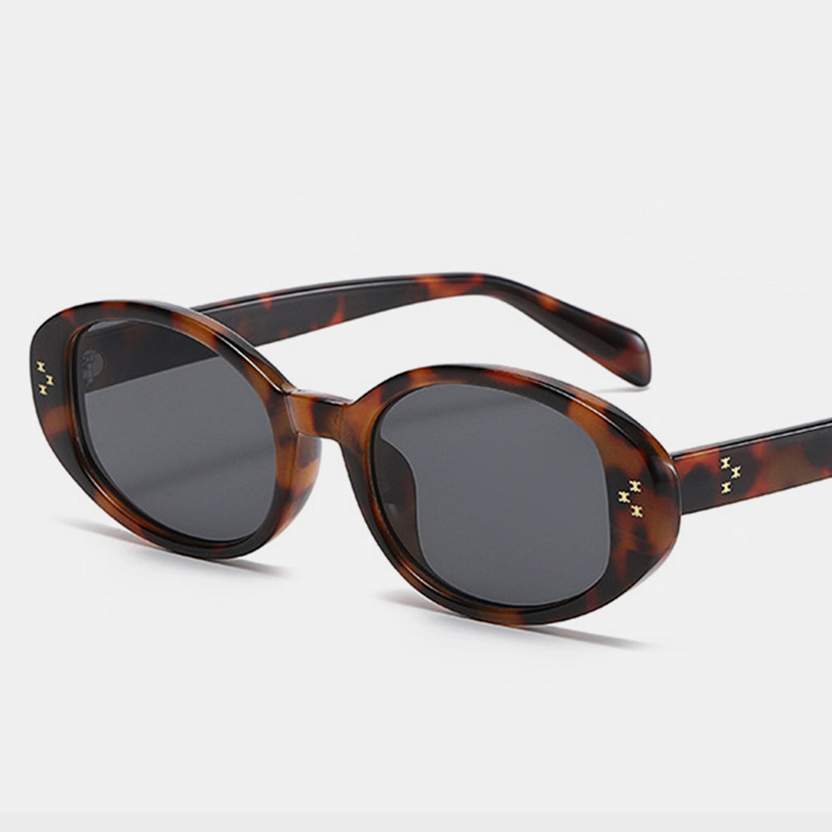 Brown tortoiseshell oval sunglasses with thick polycarbonate frames, dark lenses, softly rounded silhouette, and small star-like accents on the temples.