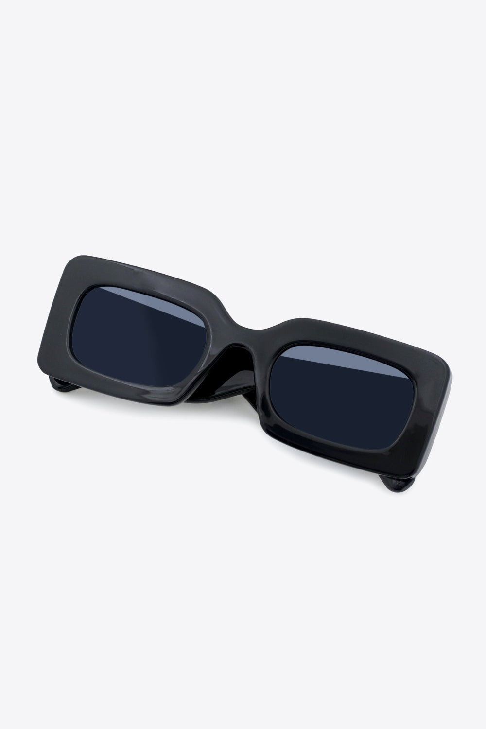 Black polycarbonate rectangle sunglasses feature softly rounded dark lenses, a bold glossy frame, and substantial sculptural temples in an angled view.