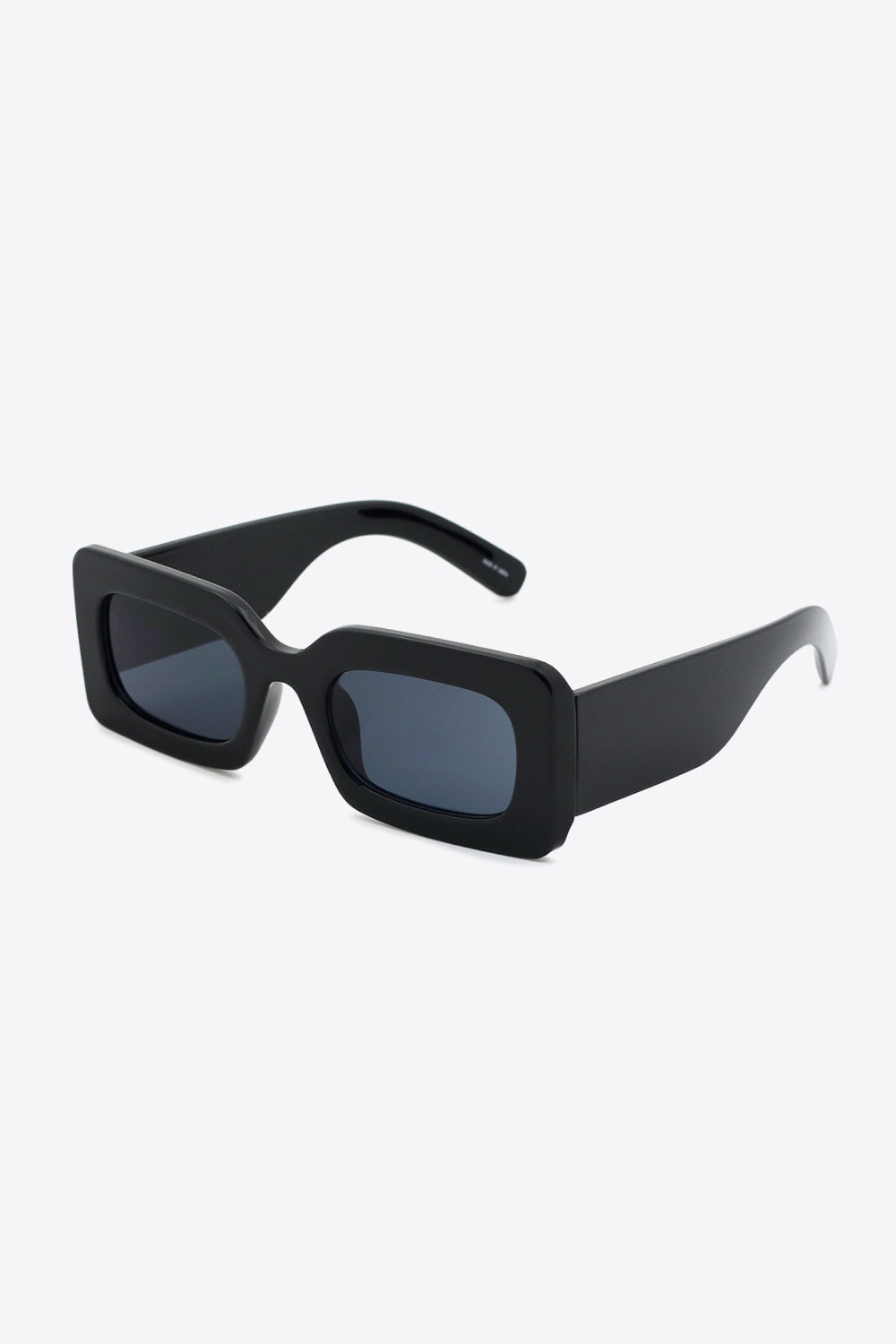 Black polycarbonate rectangle sunglasses feature softly rounded dark lenses, a bold structured frame, and substantial sculptural temples.