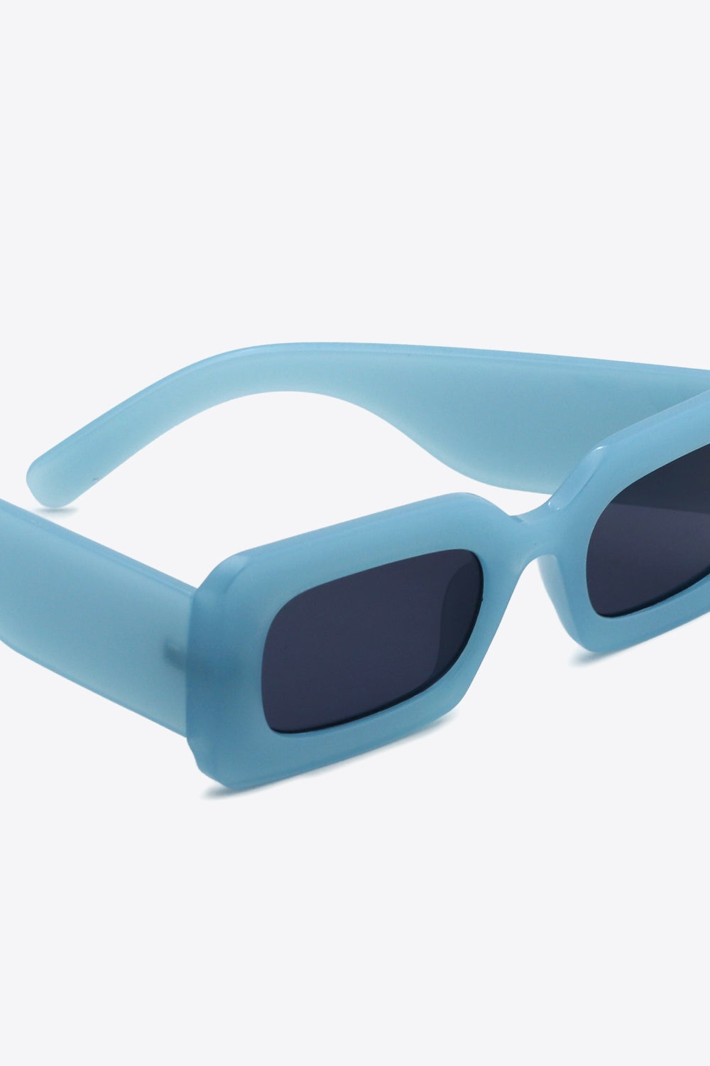 Close-up of translucent blue polycarbonate rectangle sunglasses with softly rounded dark lenses, a bold structured frame, and substantial sculptural temples.
