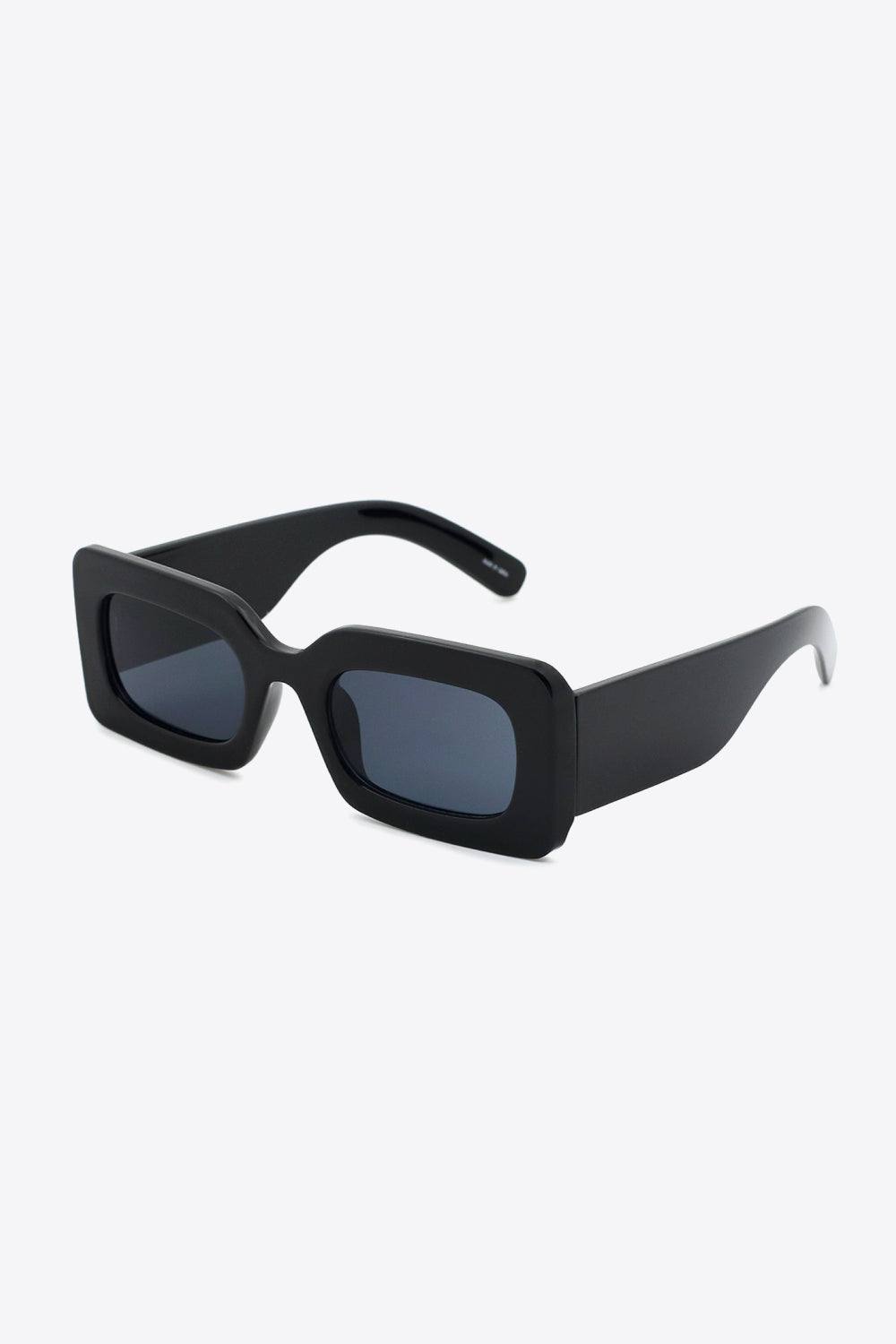 Black polycarbonate rectangle sunglasses feature softly rounded dark lenses, a bold structured frame, and substantial sculptural temples.
