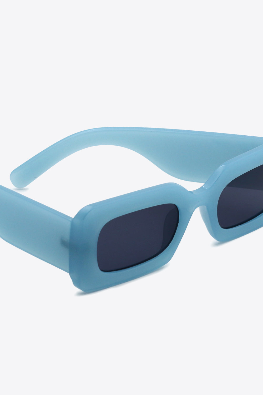 Close-up of translucent blue polycarbonate rectangle sunglasses with softly rounded dark lenses, a bold structured frame, and substantial sculptural temples.
