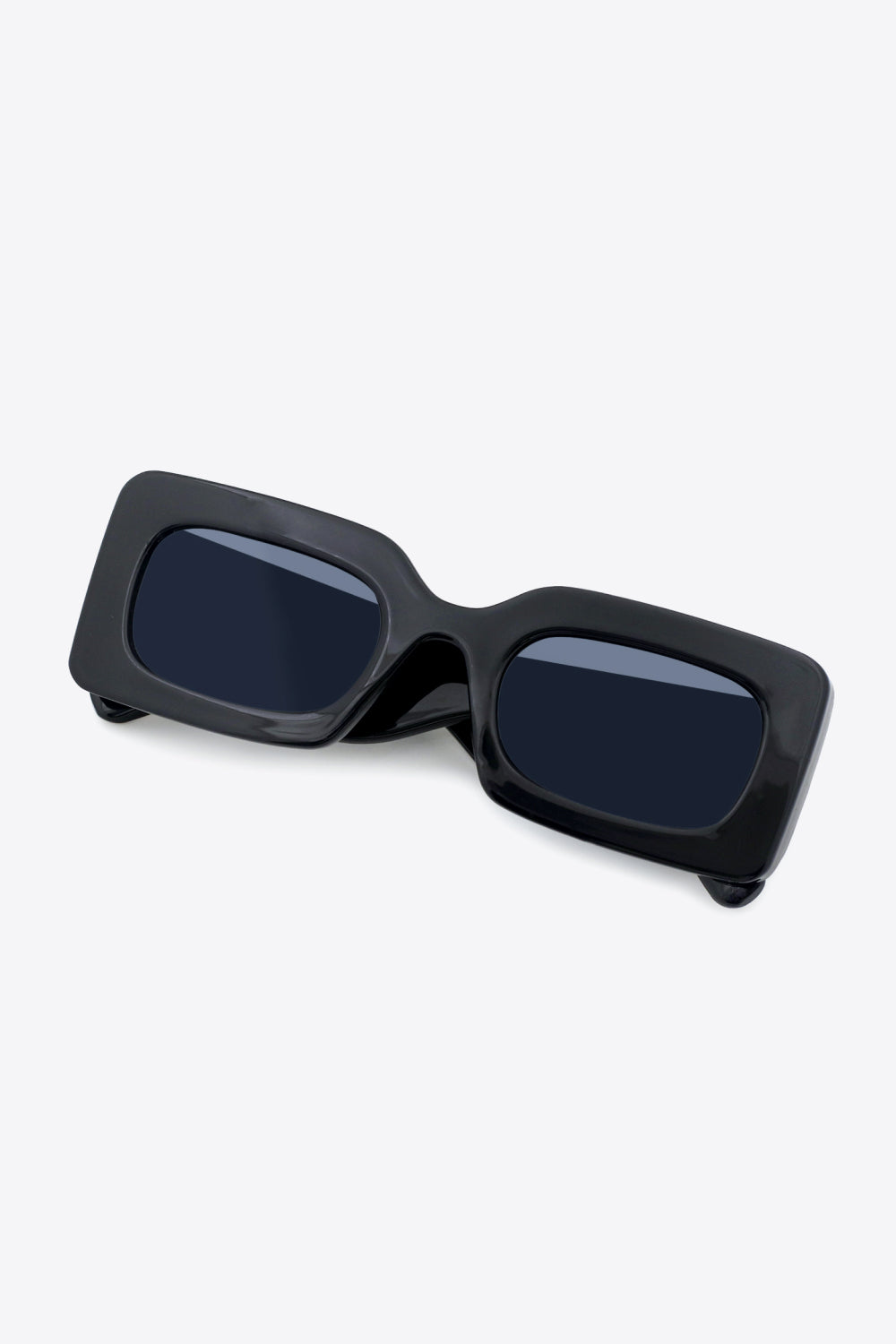 Black polycarbonate rectangle sunglasses feature softly rounded dark lenses, a bold glossy frame, and substantial sculptural temples in an angled view.