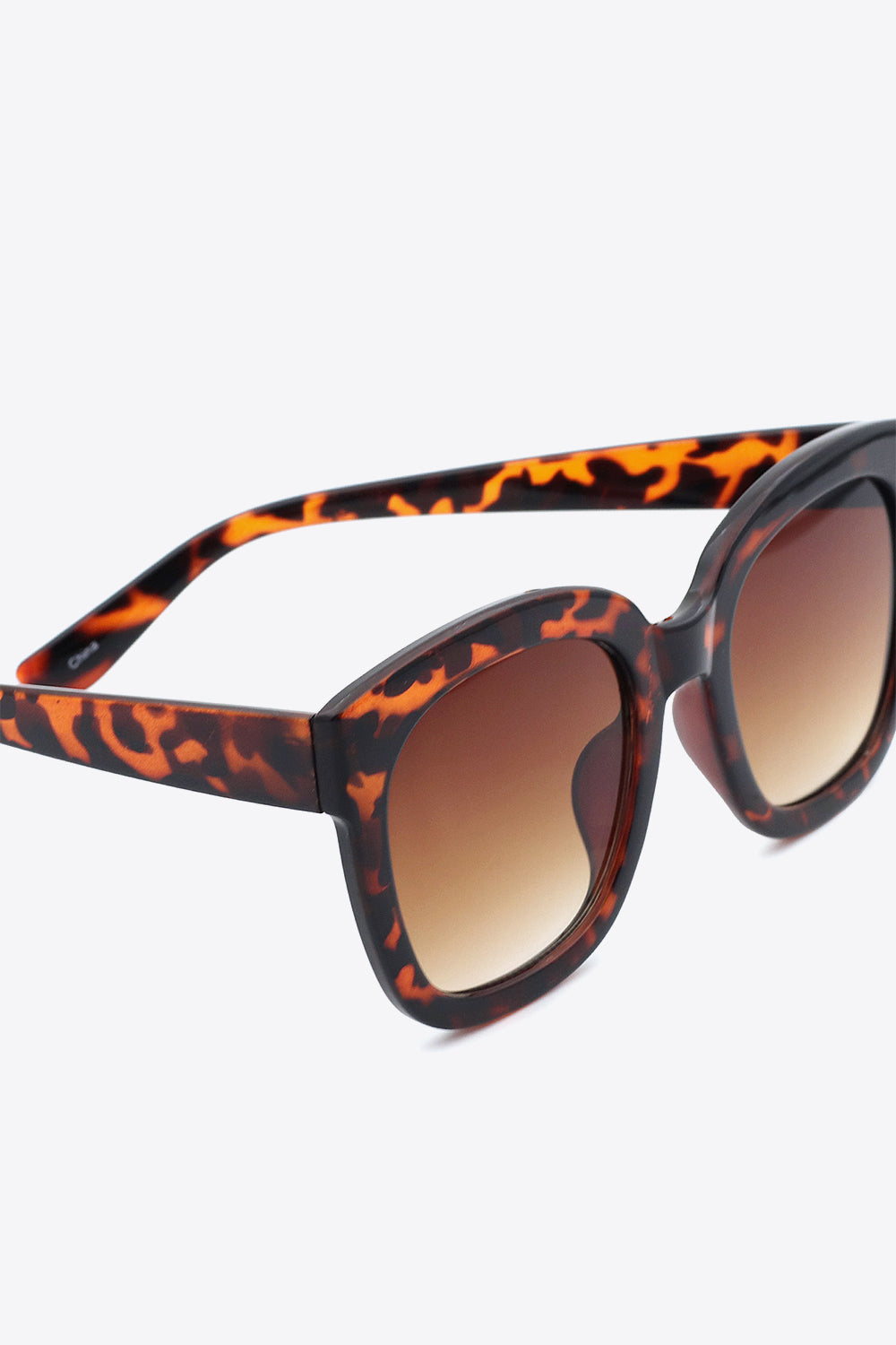 Close-up of bold square sunglasses with softly rounded tortoiseshell polycarbonate frames, matching temples, and oversized brown gradient lenses.