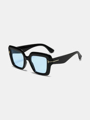 Black polycarbonate square sunglasses feature softly rounded frames, broad temples, blue-tinted lenses, and subtle gold-tone hinge accents.