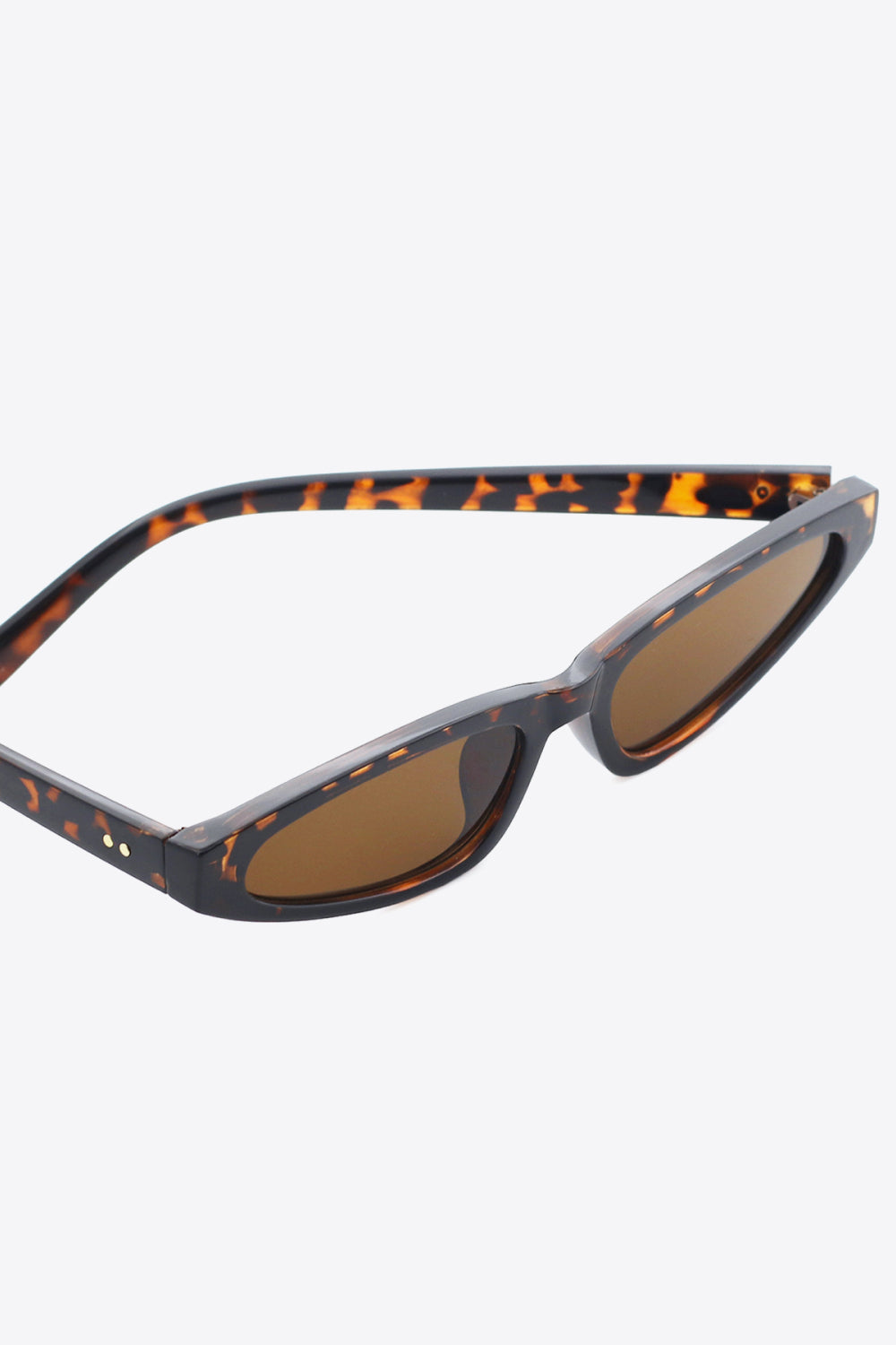 Tortoiseshell polycarbonate cat-eye sunglasses feature a gently upswept silhouette, structured matching temples, and warm brown acetate lenses with UV400 protection.