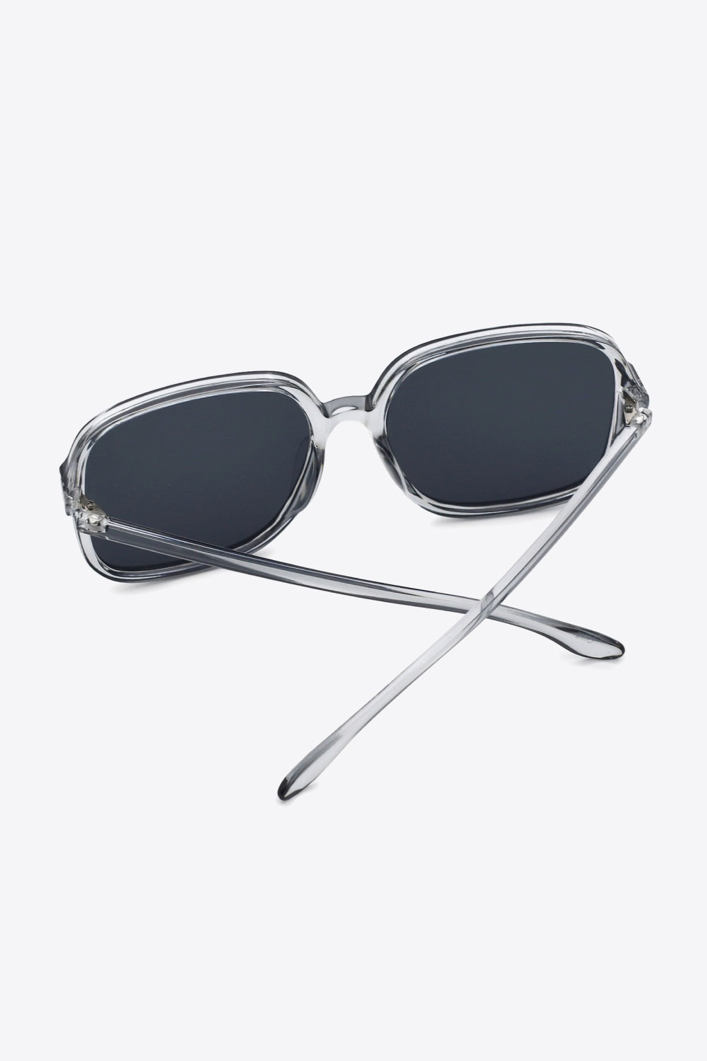 Clear polycarbonate square sunglasses feature broad dark lenses, softly rounded corners, a defined top line, and sleek temples crossed behind the frame.