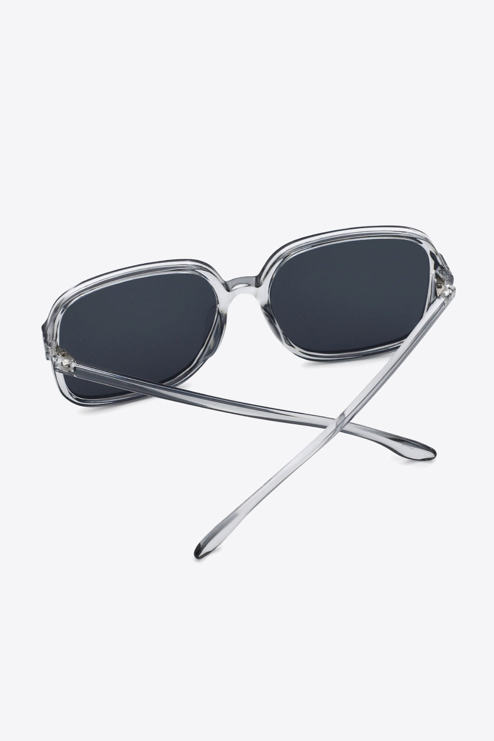 Clear polycarbonate square sunglasses feature broad dark lenses, softly rounded corners, a defined top line, and sleek temples crossed behind the frame.