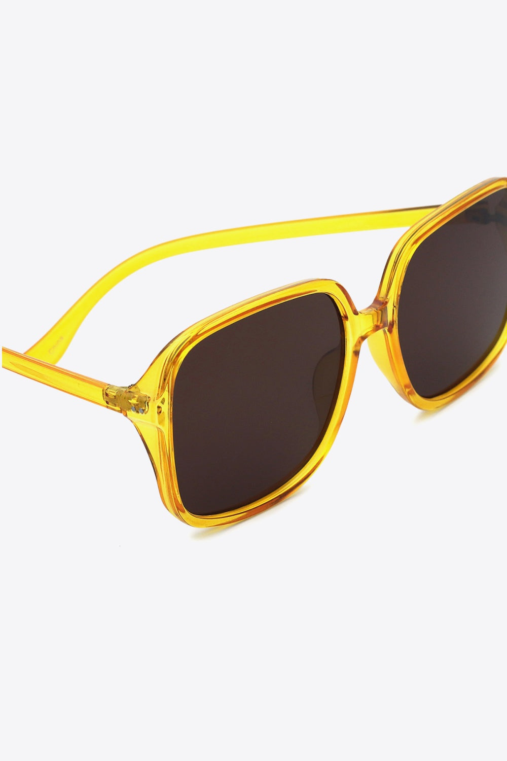 Close-up of square sunglasses with a translucent yellow polycarbonate frame, softly rounded corners, broad dark lenses, and sleek matching temples.