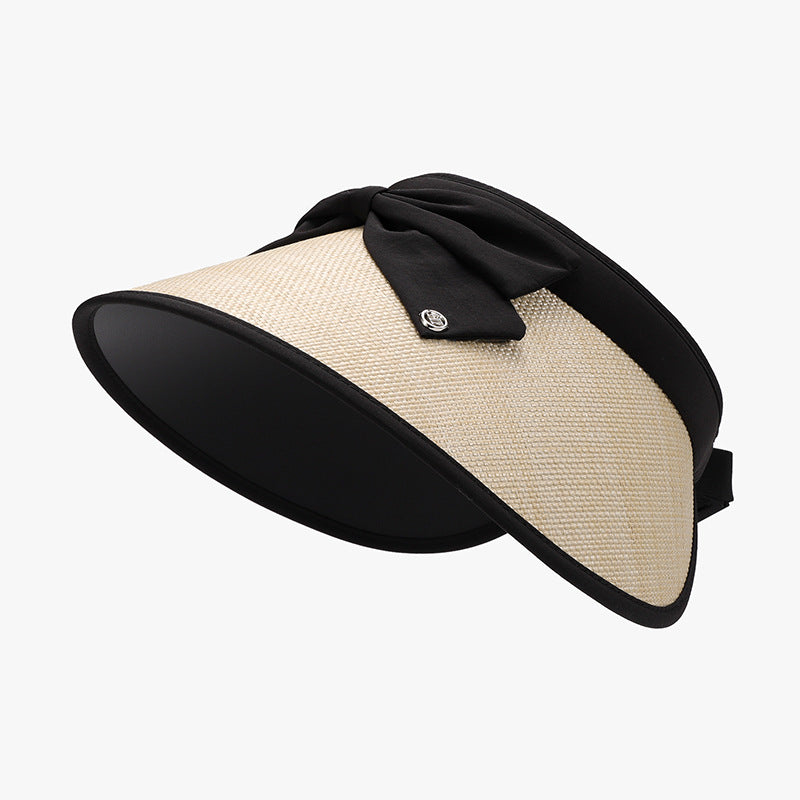 A woven polyester sun hat features a natural grass-colored curved visor, generous black-trimmed brim, open-back band, and softly gathered bow at the crown.