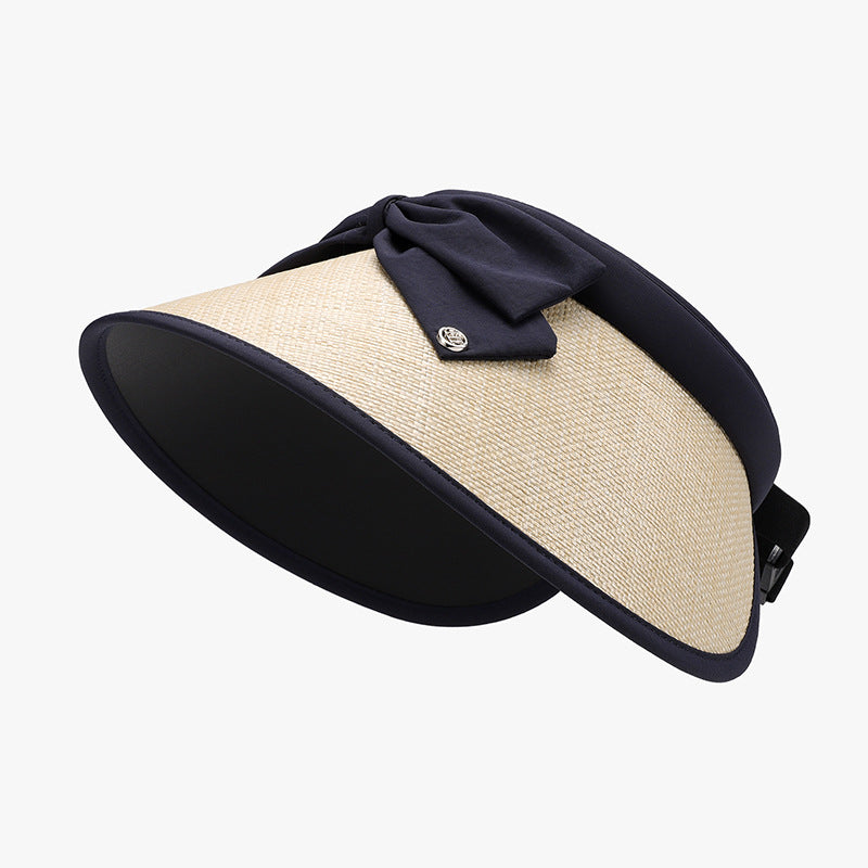A natural-toned woven adjustable sun hat features a curved visor, generous wide brim, navy trim, and a softly gathered bow at the crown.