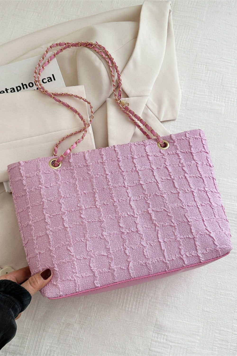 A hand holds a medium pink polyester textured tote with a softly structured silhouette, linked chain handles, and gold-tone ring accents.