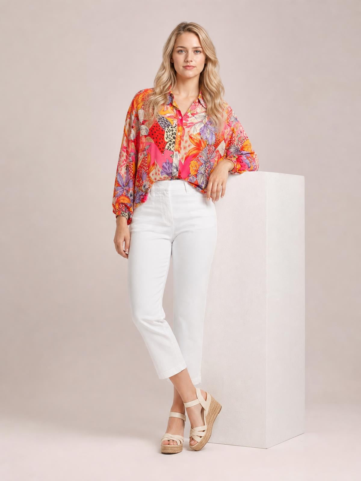 Model wears a vibrant printed button-down shirt with long sleeves, a collared neckline, front buttons, and a relaxed silhouette while leaning casually.