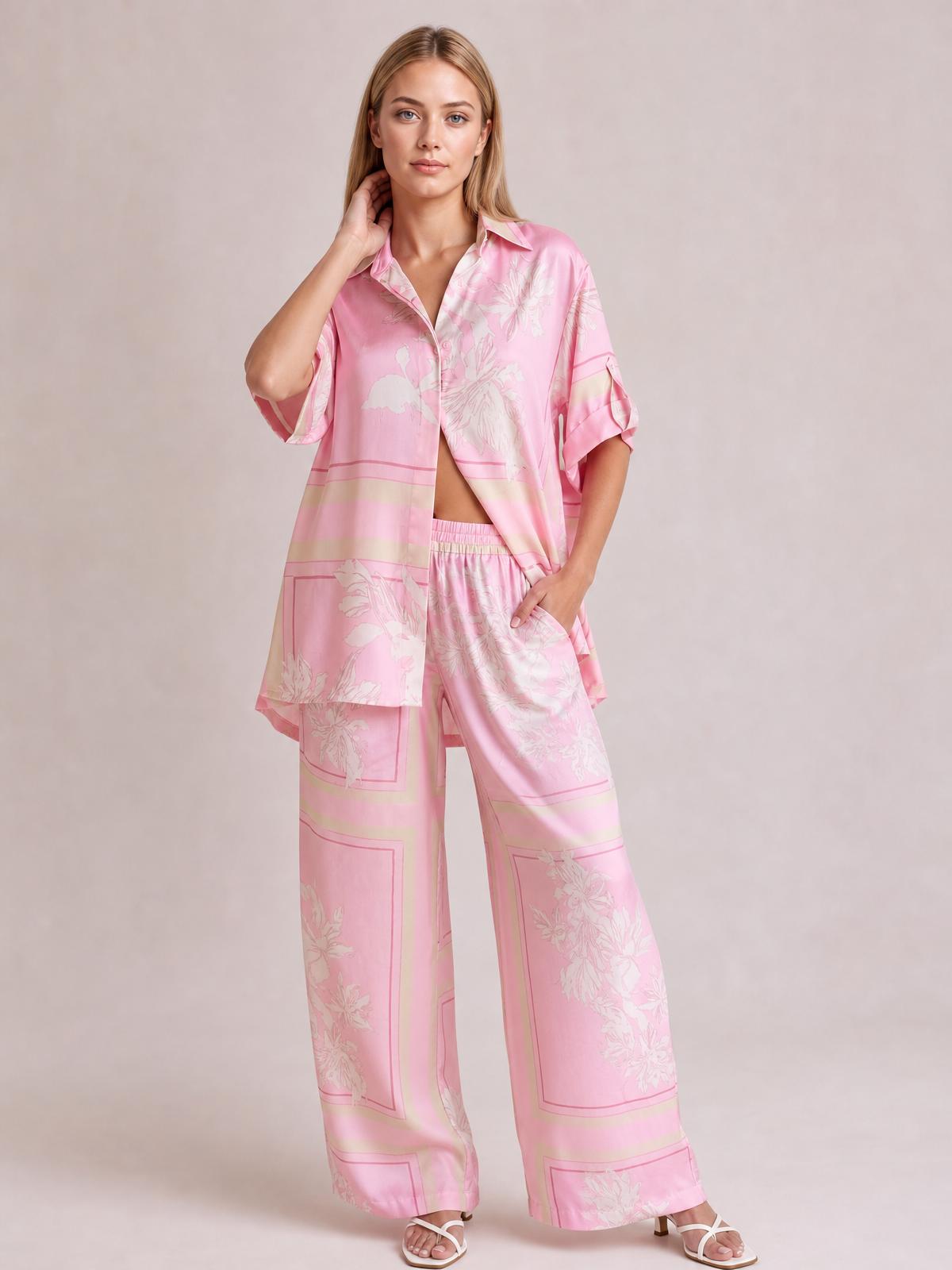 A model poses in a pink floral printed button-up shirt and wide-leg pants set, featuring short sleeves, a relaxed silhouette, and a hand tucked into a pocket.