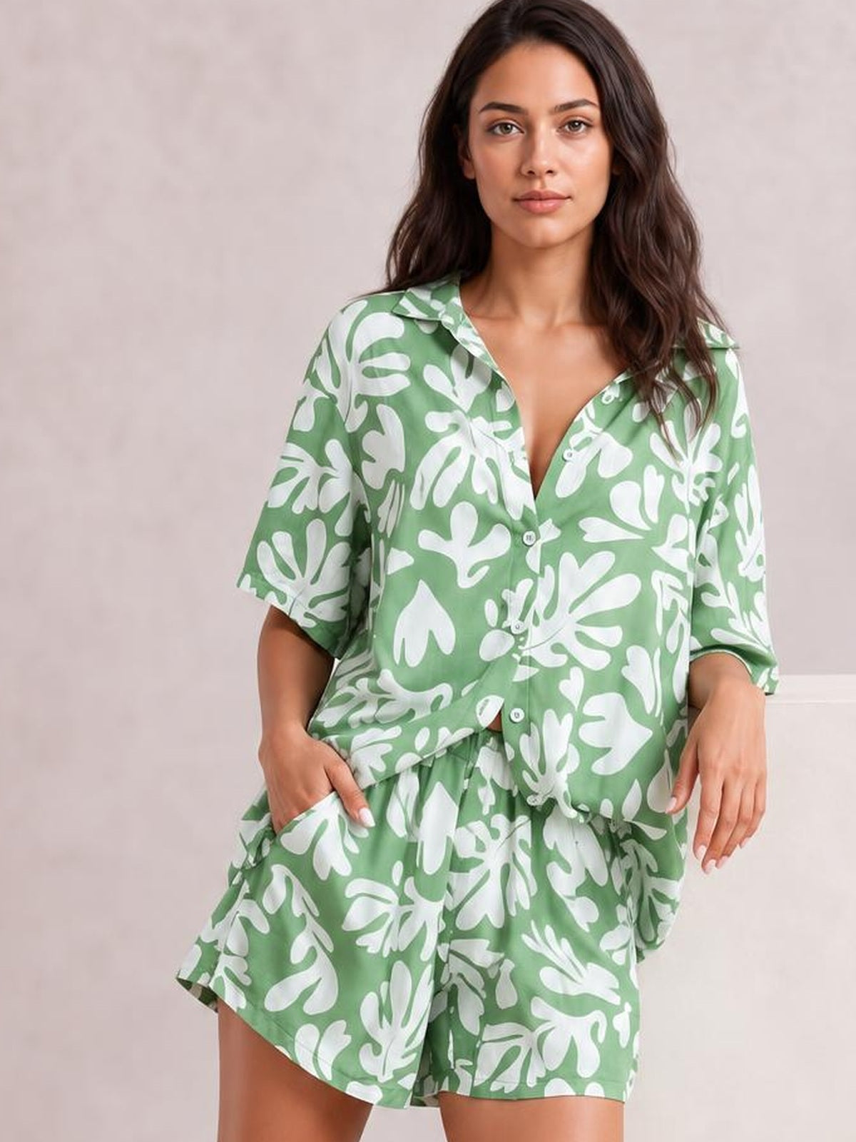 Model poses in a green and white printed button-up shirt and shorts set, featuring a relaxed silhouette, short sleeves, and pocketed shorts.