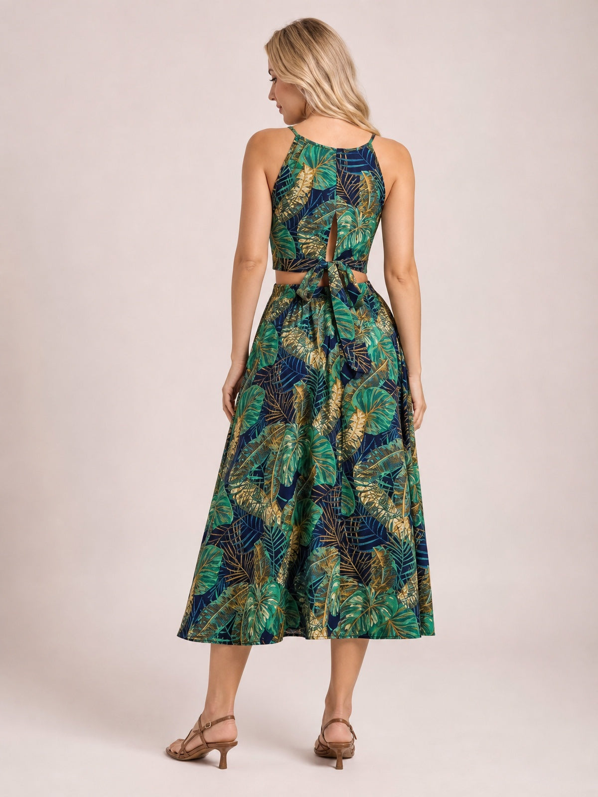 A model poses with her back turned in a navy tropical-print cami and midi skirt set, featuring slender straps, a tied back, and a full flared silhouette.