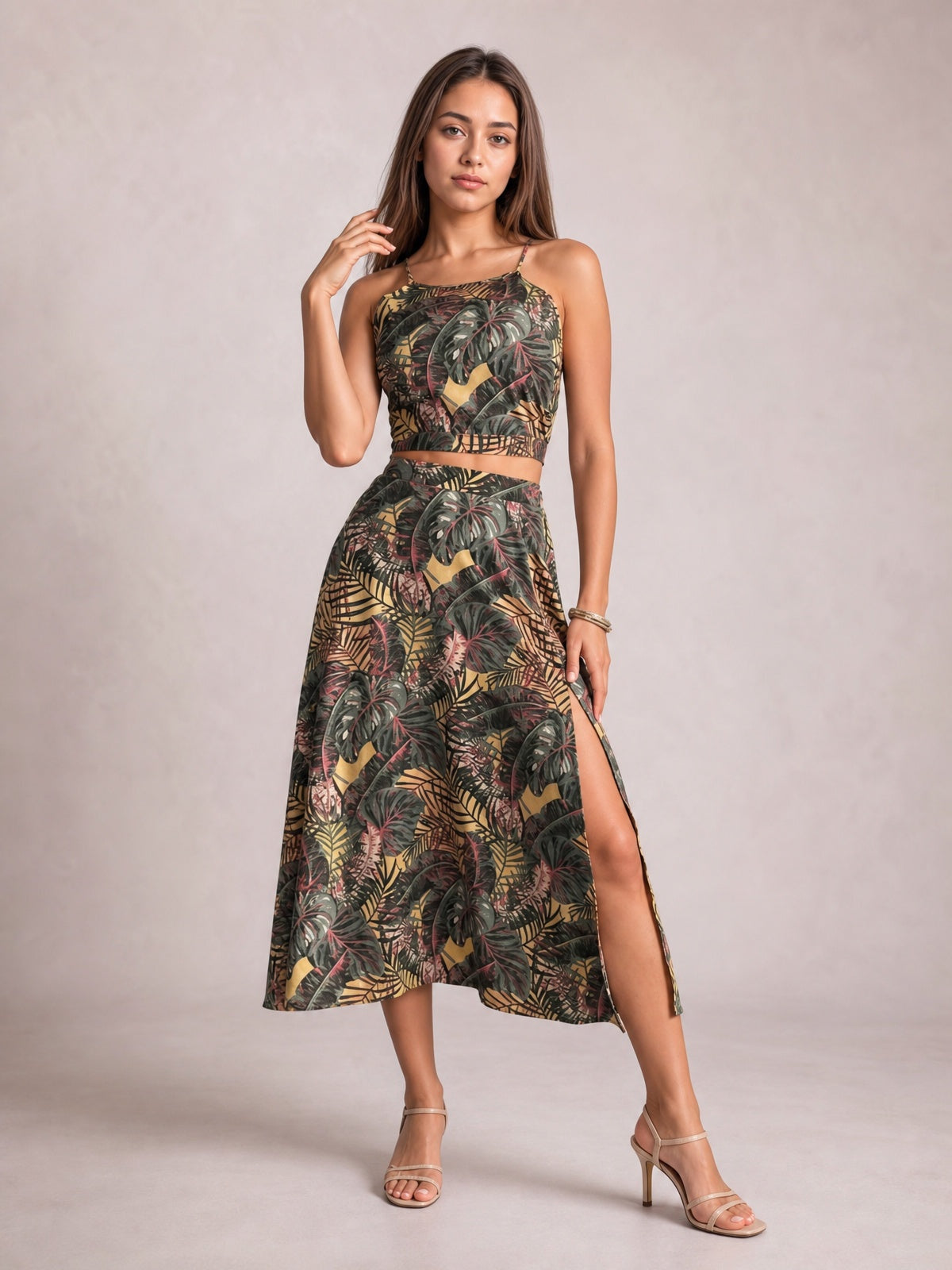 Model poses in a printed cami and high-waisted midi skirt set with slender straps, a cropped silhouette, tropical pattern, flared shape, and side slit.