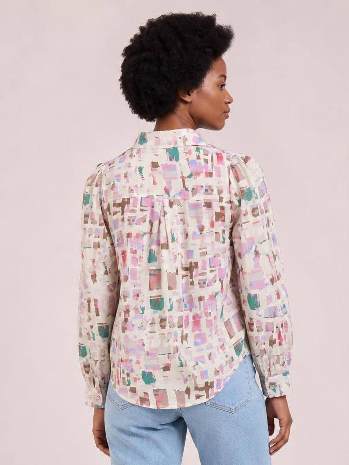 A model poses in profile wearing a pastel printed collared neck long sleeve shirt with a relaxed silhouette, back yoke, button cuffs, and curved hem.