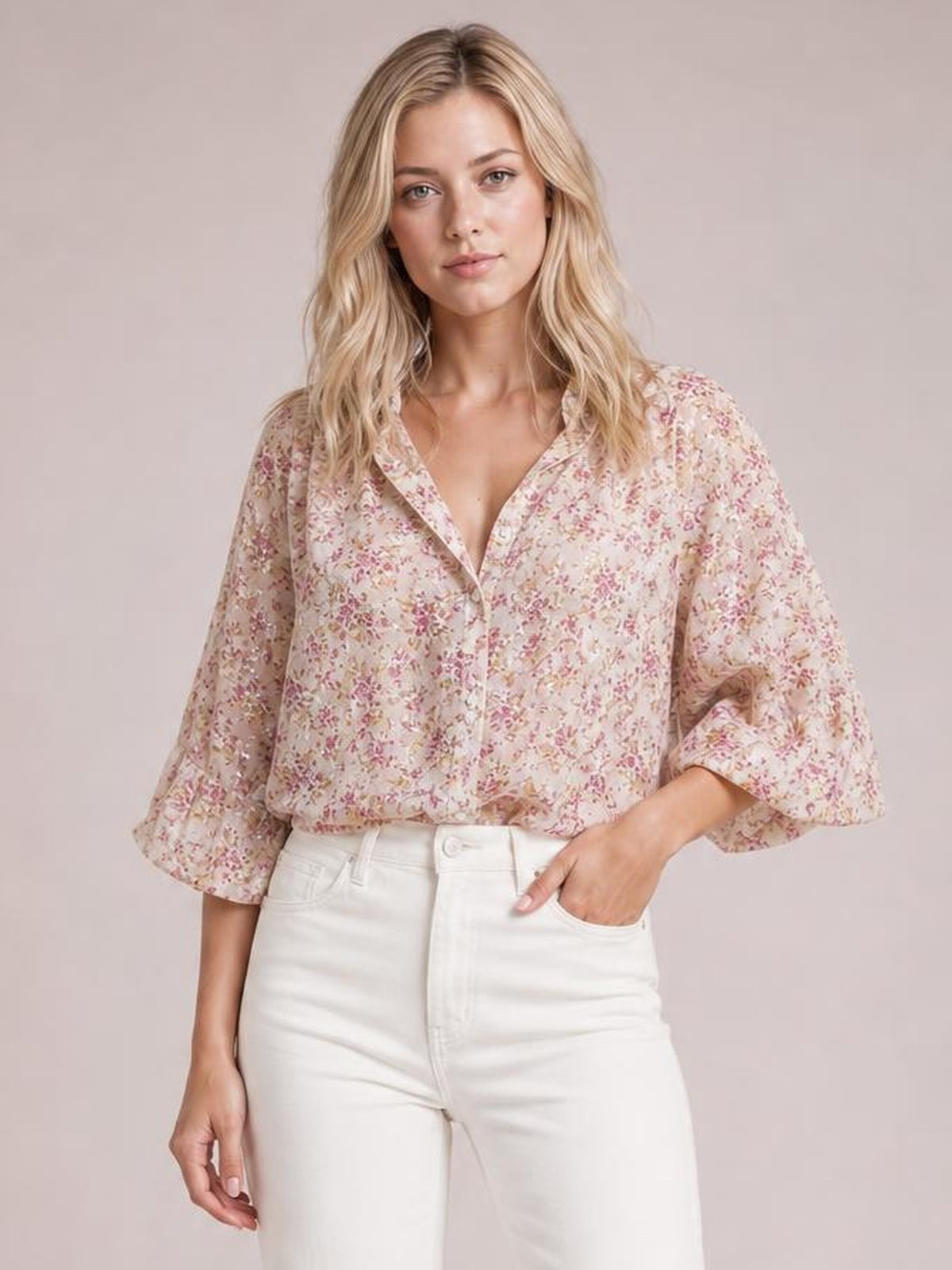 Model poses in a pink and cream floral printed collared neck long sleeve shirt with a relaxed silhouette, button front, and rolled cuffs.