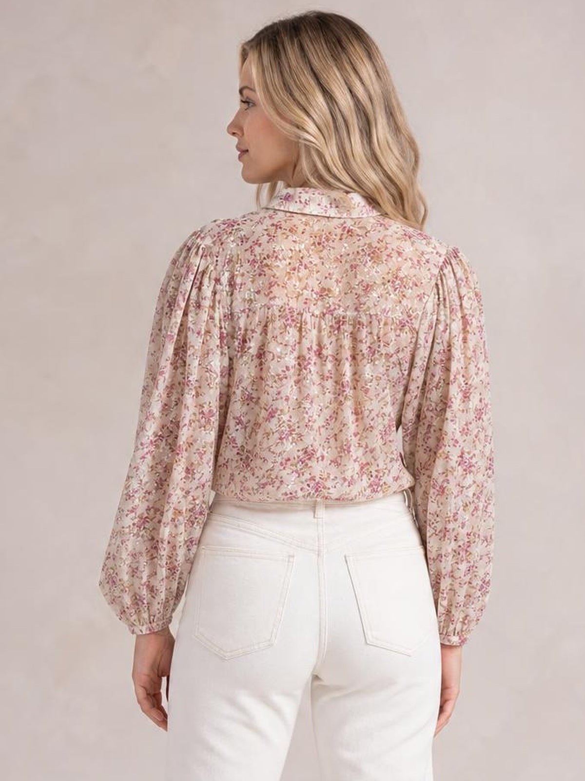 A model poses from the back in a cream floral printed collared shirt with long puff sleeves, gathered shoulder seams, and a relaxed waist-length silhouette.