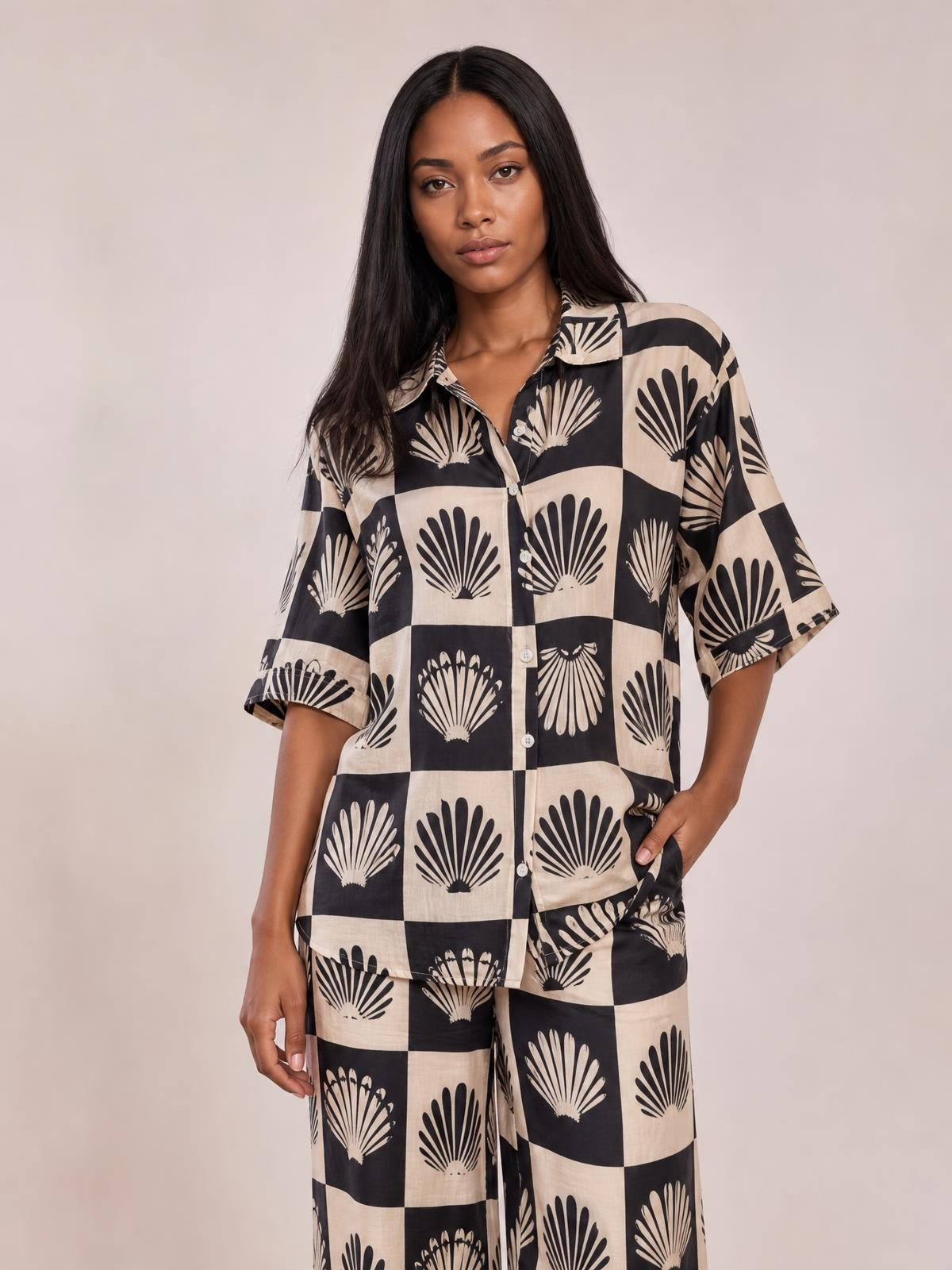 Model wears a black printed collared top with button front and pockets, paired with matching flowing wide-leg pants in a relaxed silhouette.