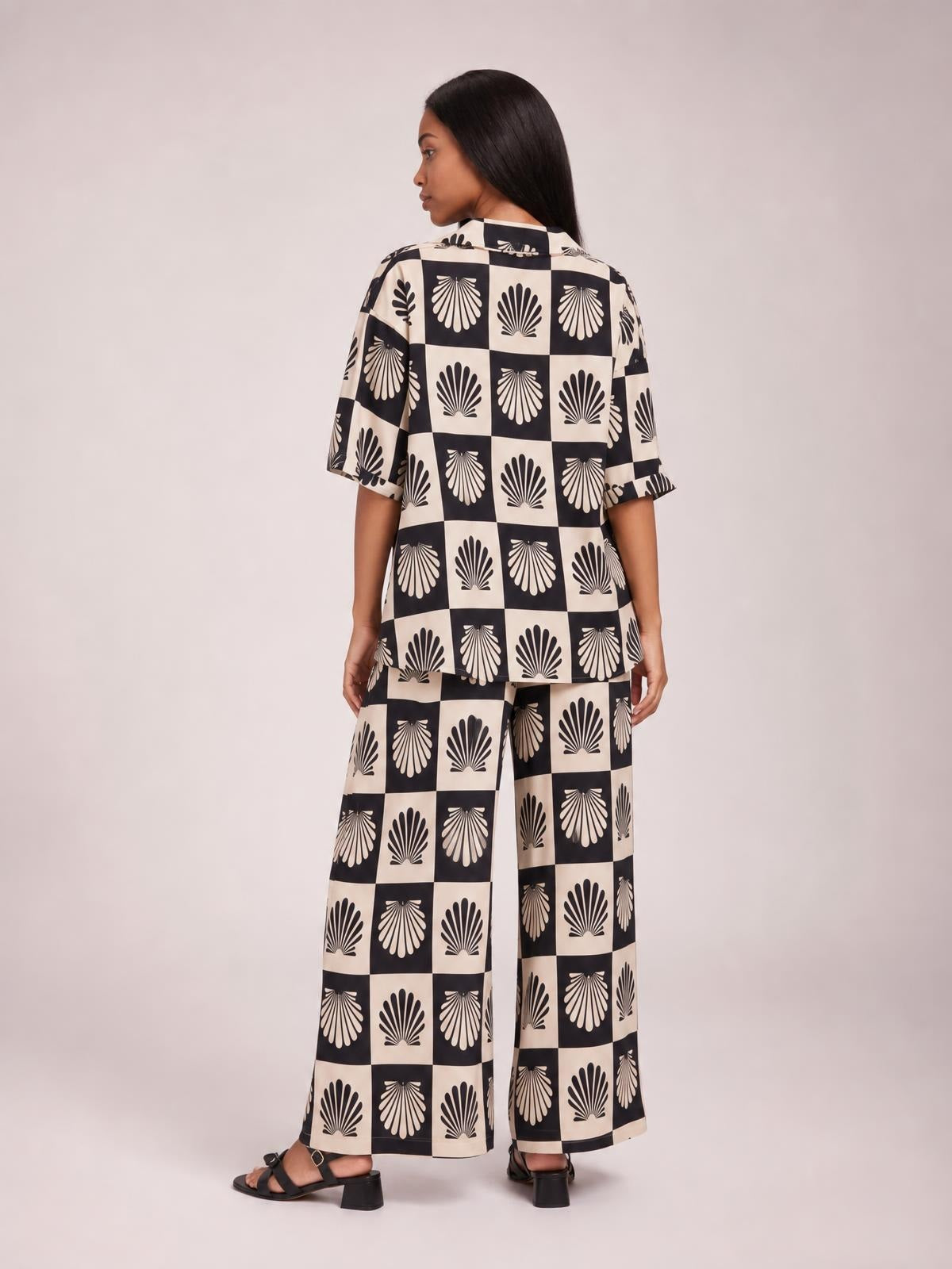 Model turned away in a black-and-cream printed collared buttoned top and matching wide-leg pants set, showing the relaxed silhouette and short sleeves.