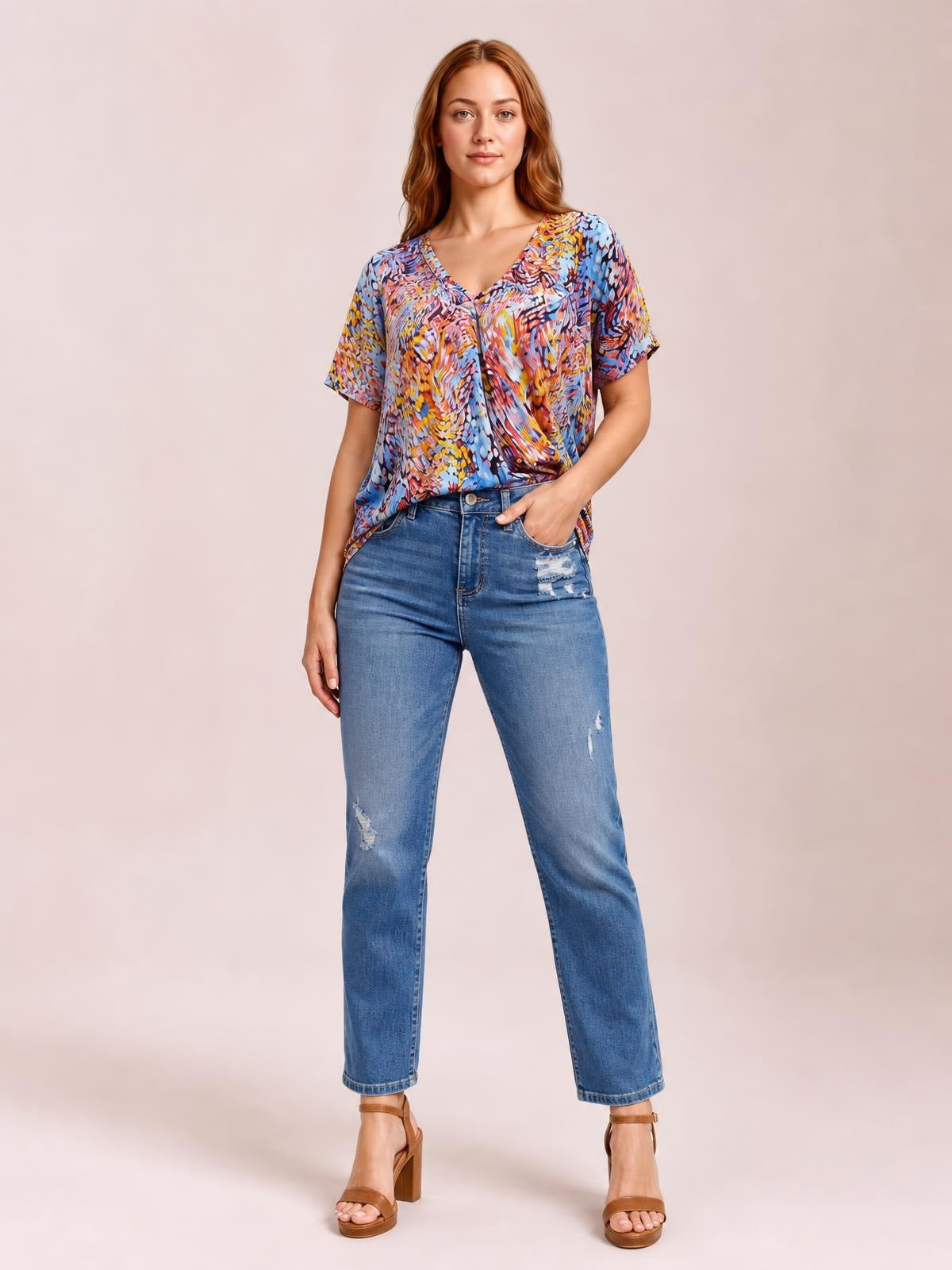 Model stands with one hand in her pocket wearing a multicolored printed dolman top with a V-neck, short sleeves, and a relaxed flowy silhouette.