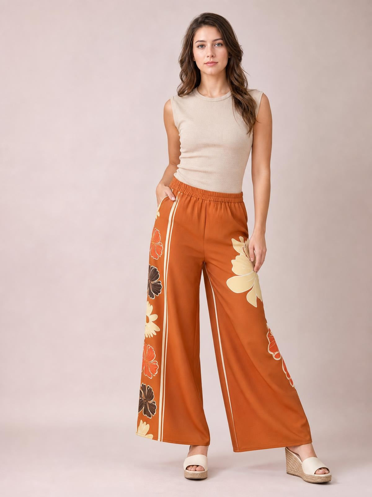 Model poses in orange printed elastic waist wide leg pants with floral side panels and double stripe trim, featuring a relaxed full-length silhouette.