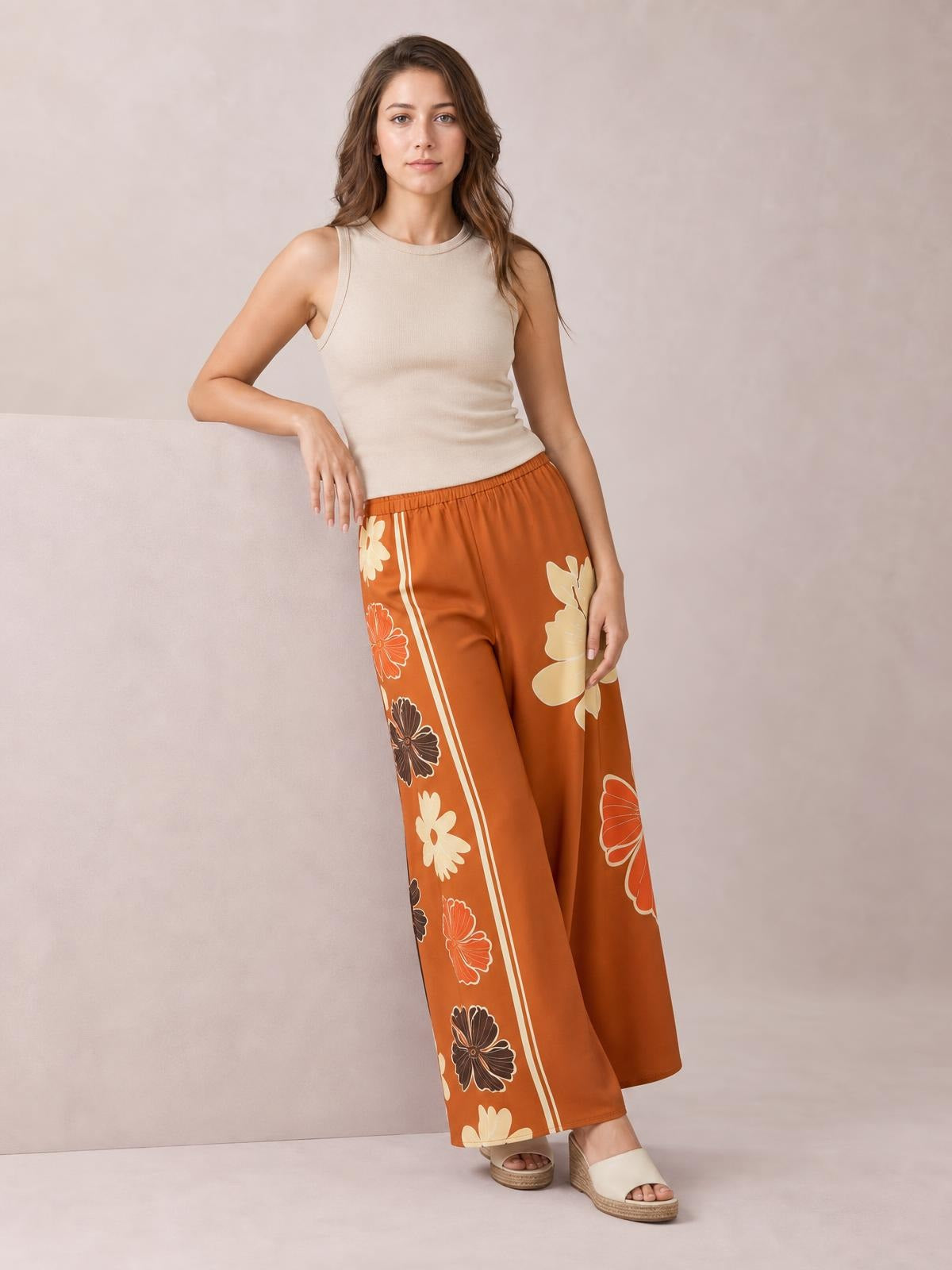 Model wearing rust-orange printed elastic waist wide leg pants with floral side panels, a flowing silhouette, and ankle-length hems.