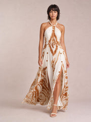 Model in a white and brown printed halter neck maxi dress with a gathered bodice, flowing silhouette, and high front slit.