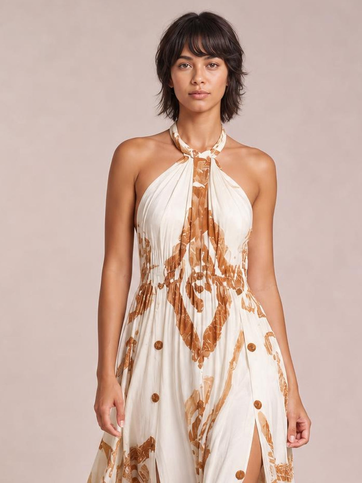 Model standing in a printed halter neck maxi dress with a cream base, brown abstract pattern, gathered pleats, flowing silhouette, and front slit.