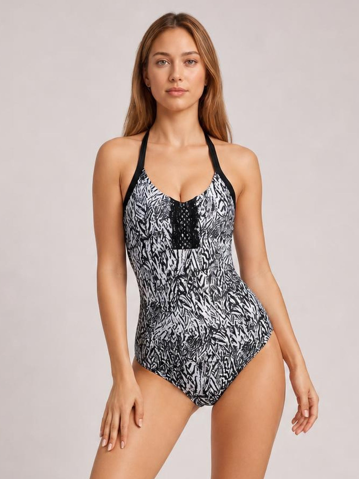 Model poses in a black-and-white printed halter neck one-piece swimsuit with tied straps, a fitted silhouette, and a scoop neckline.