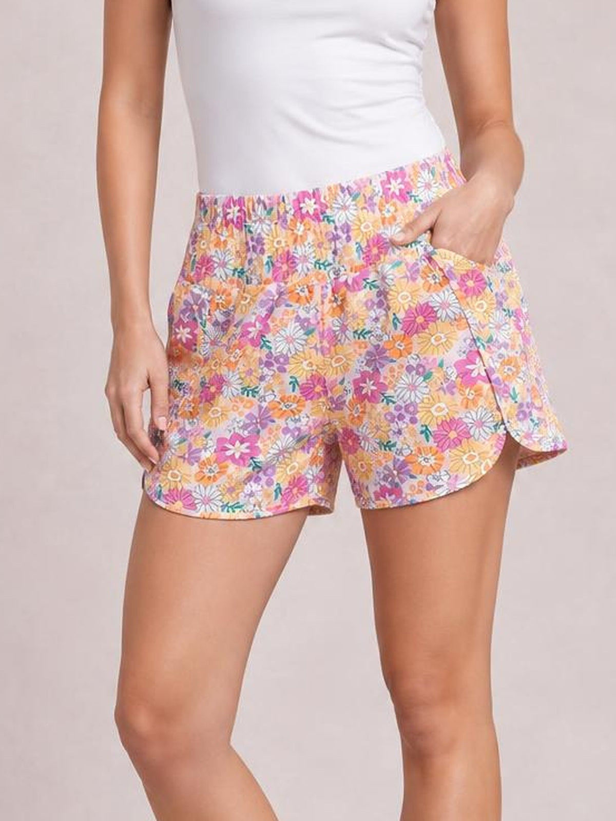 A model poses in colorful floral-print high-waist shorts with a gathered elastic waistband, relaxed silhouette, curved hems, and side pockets.