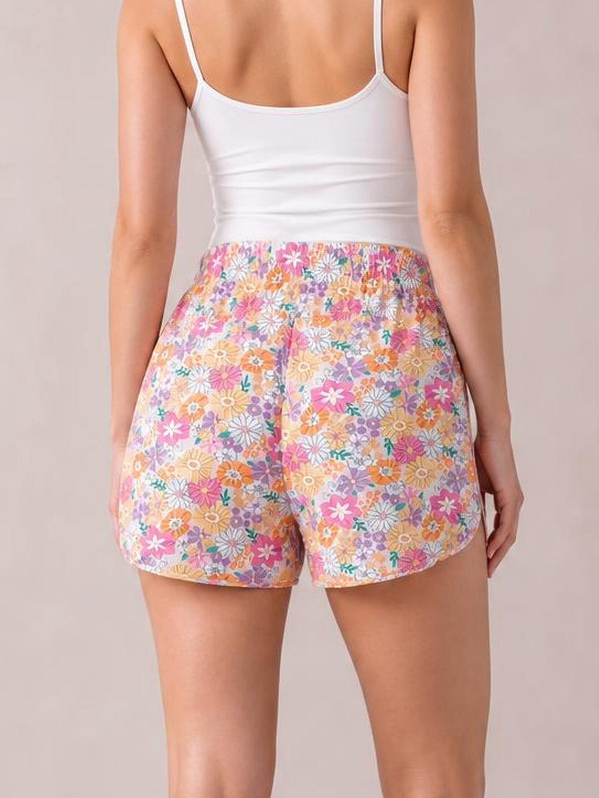 Model shown from behind wearing high-waist shorts with a colorful floral print, curved hems, and a relaxed silhouette.