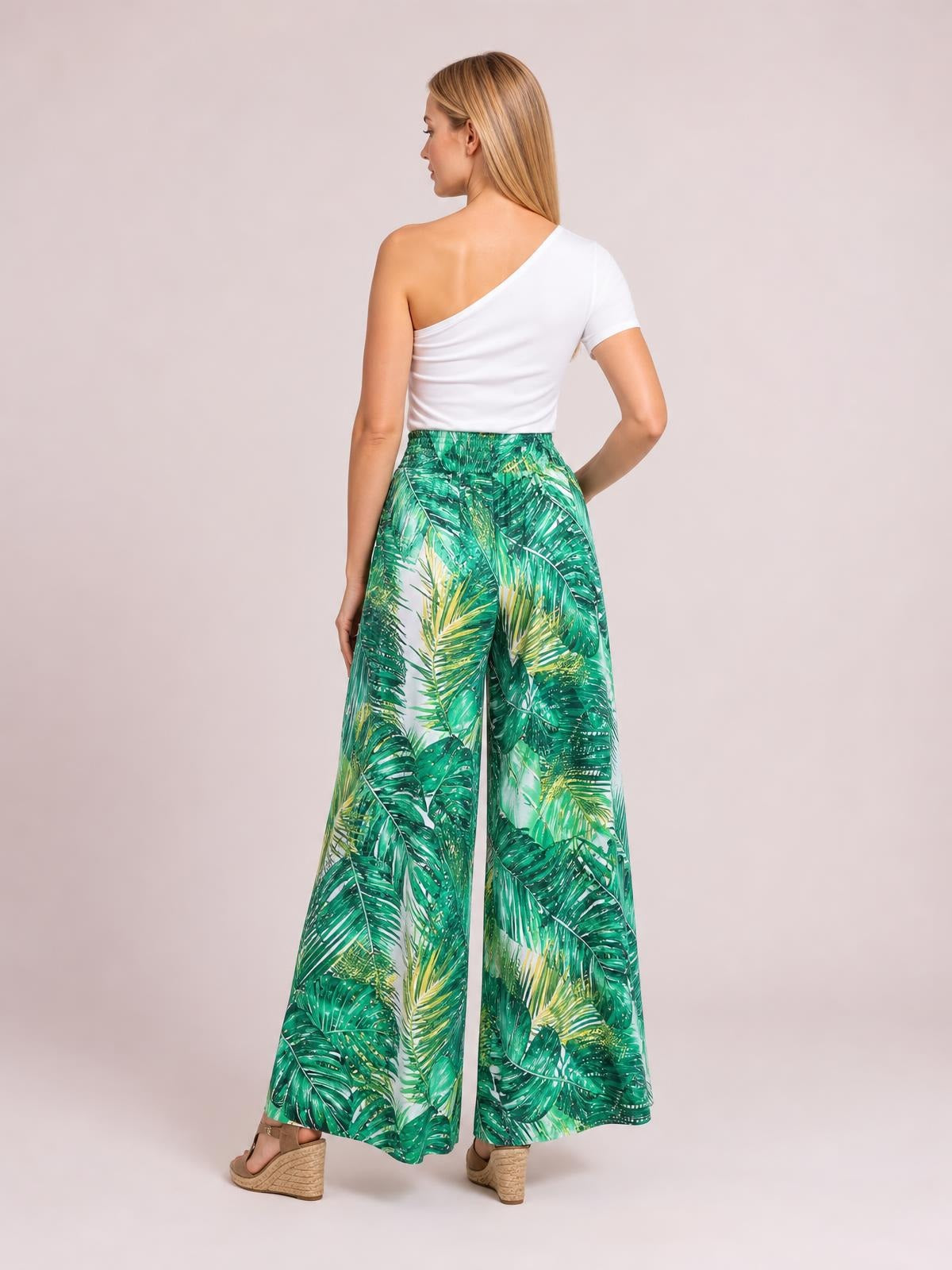 Model poses from the back in green printed high-waist wide-leg pants with a flowing silhouette and tropical leaf pattern.