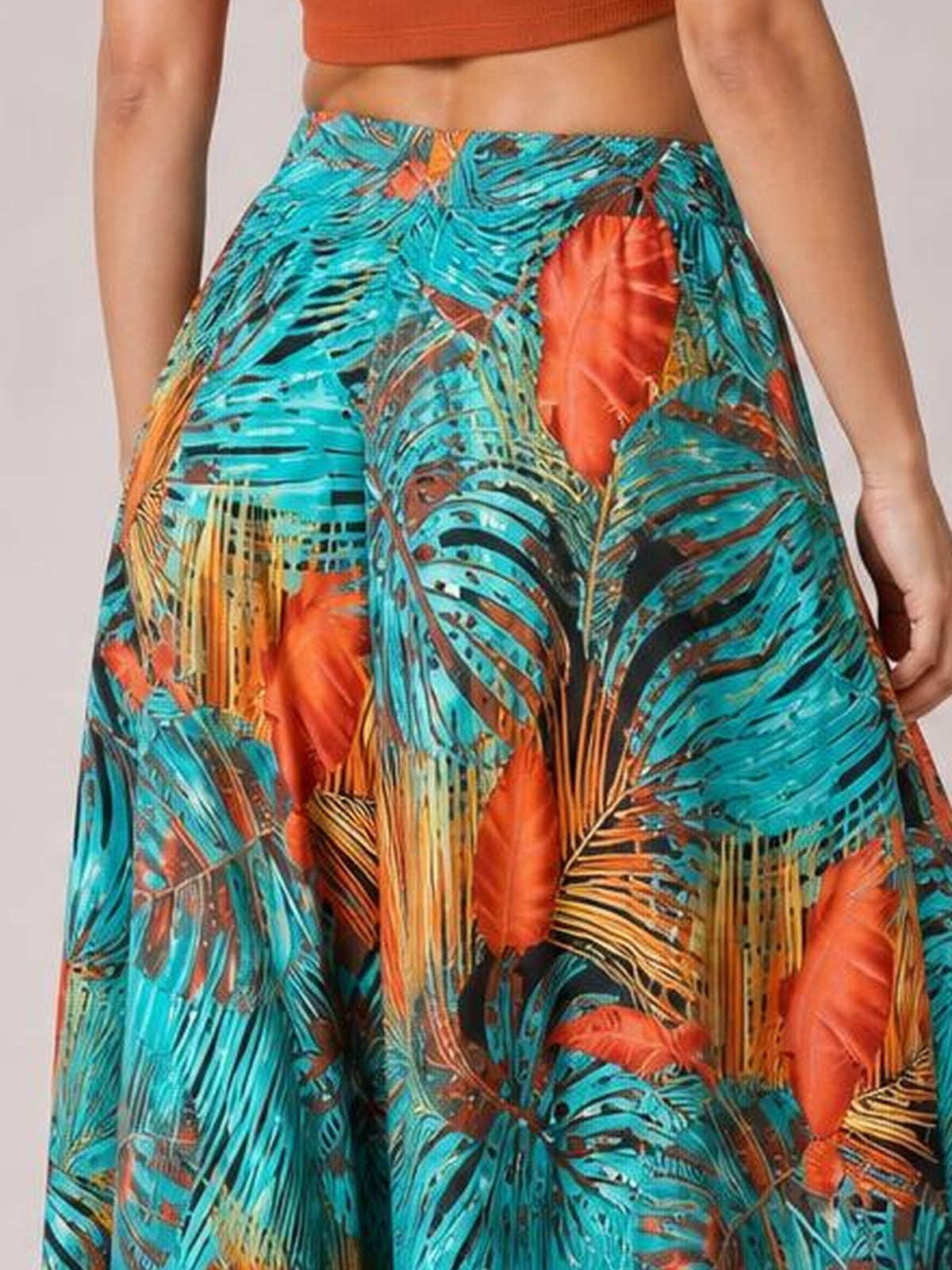 Model wearing vibrant turquoise printed high waist wide leg pants with tropical leaf motifs in orange, black, and tan, shown in a relaxed standing pose.