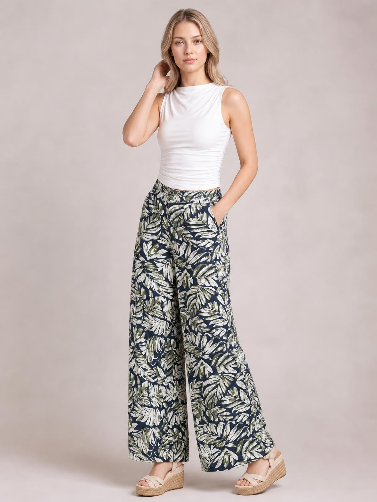 A model poses in navy printed high-waist wide-leg pants with a leafy botanical pattern, flowing silhouette, cropped hems, and hands resting at her sides.