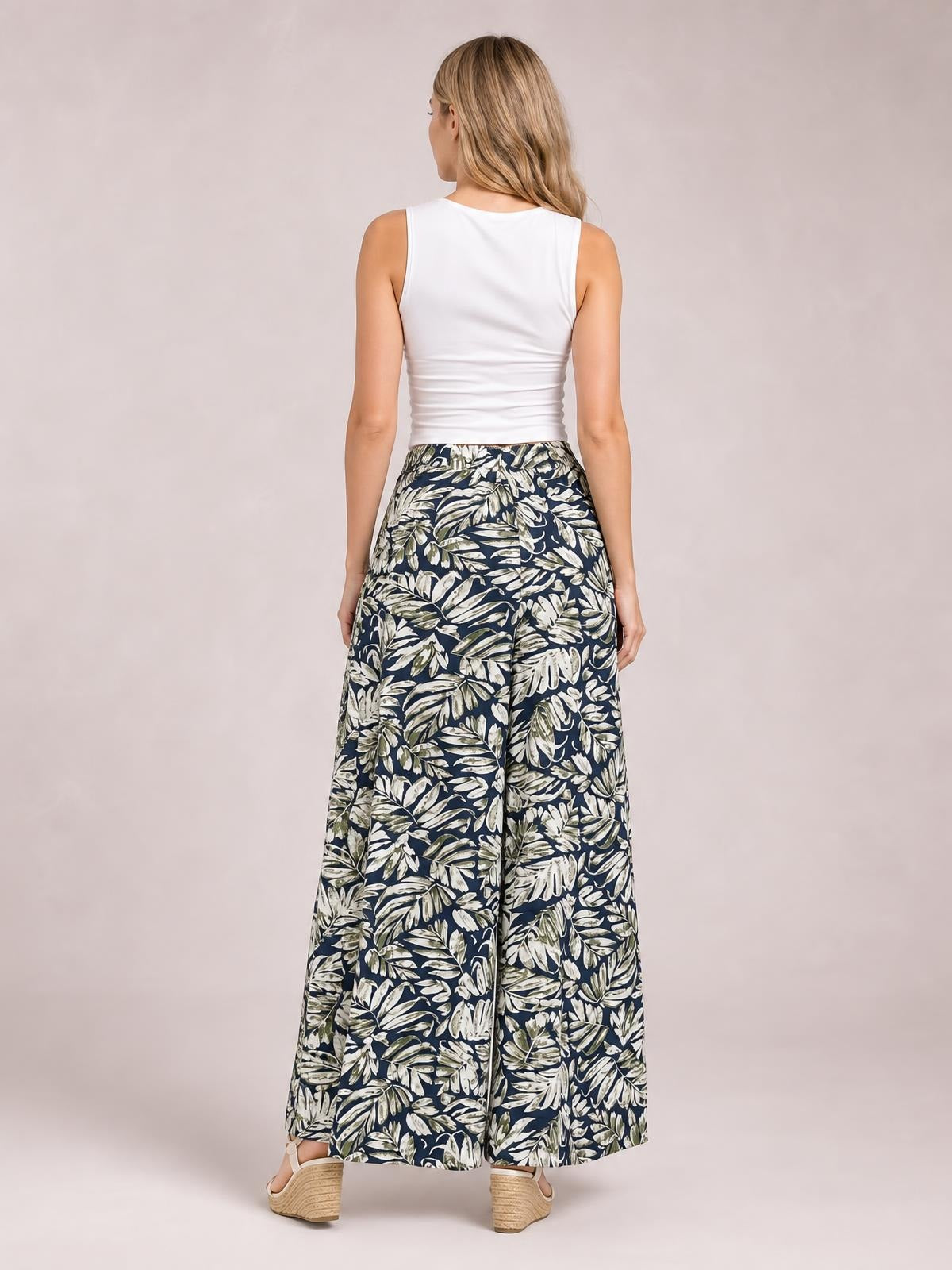 Model viewed from behind wears printed high-waist wide-leg pants in navy with a cream leaf pattern, a flowing silhouette, and wide hems.