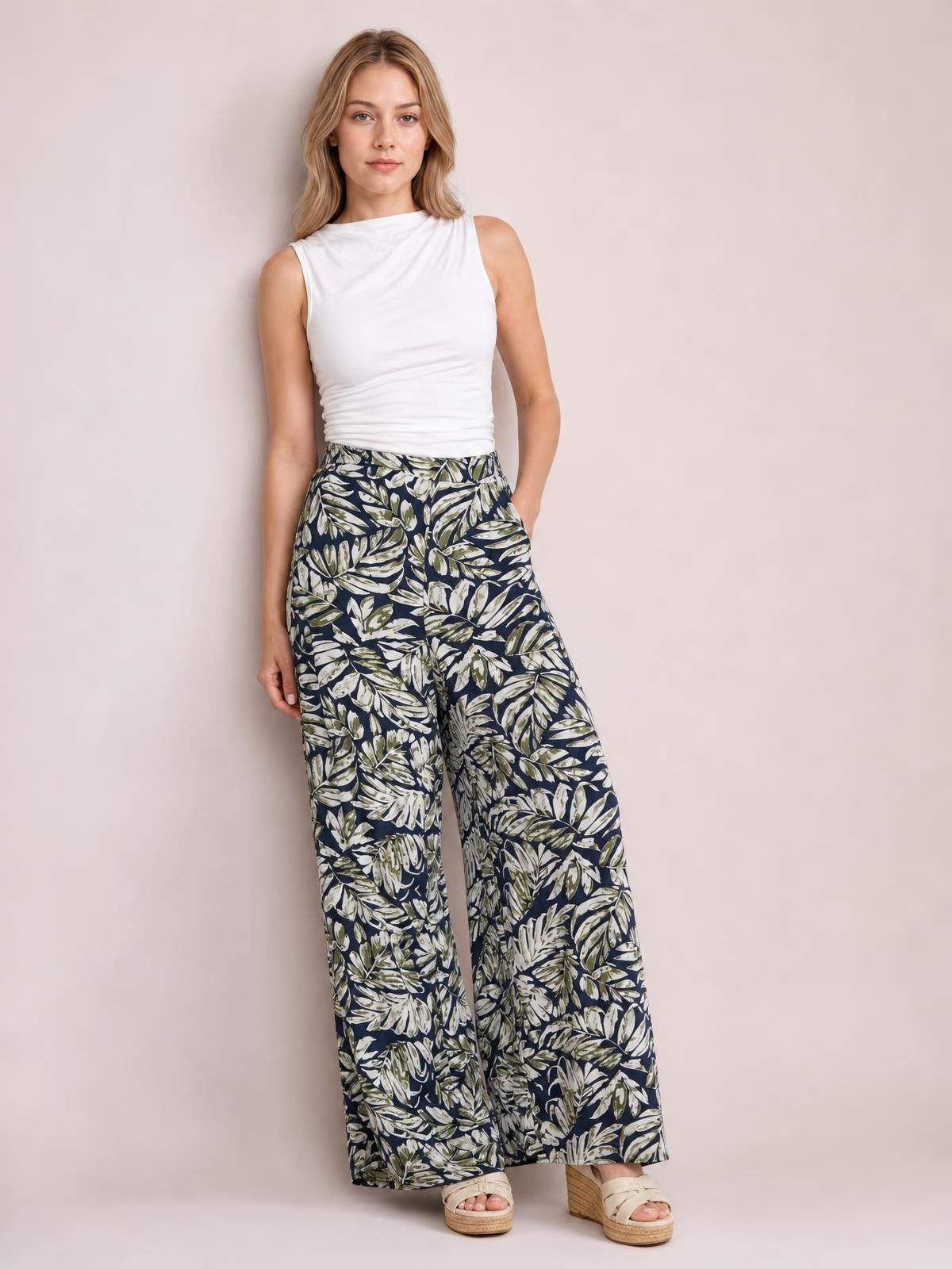 Model wearing printed high-waist wide-leg pants with a navy leafy pattern, relaxed flowing silhouette, and a hand-in-pocket pose.