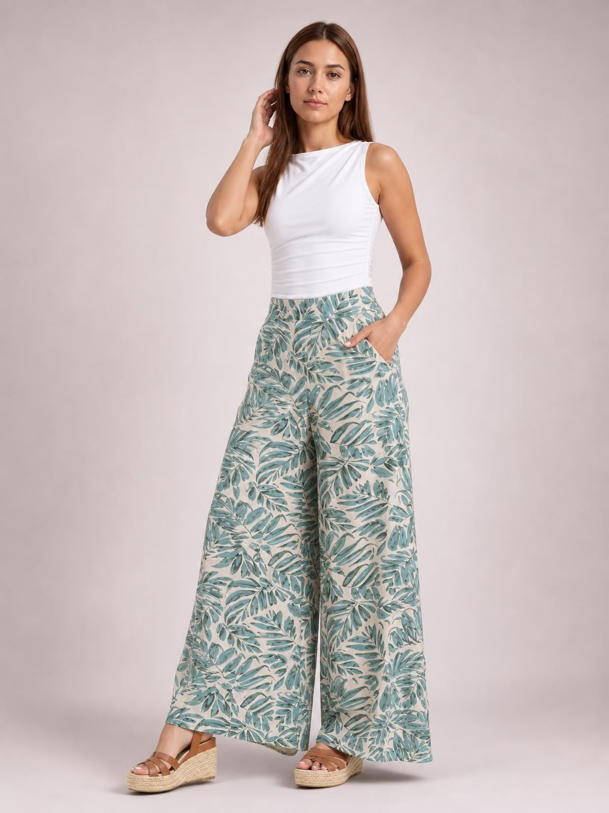 Model wearing printed high-waist wide-leg pants with a pale blue and green leaf pattern, posing with one hand in a pocket.