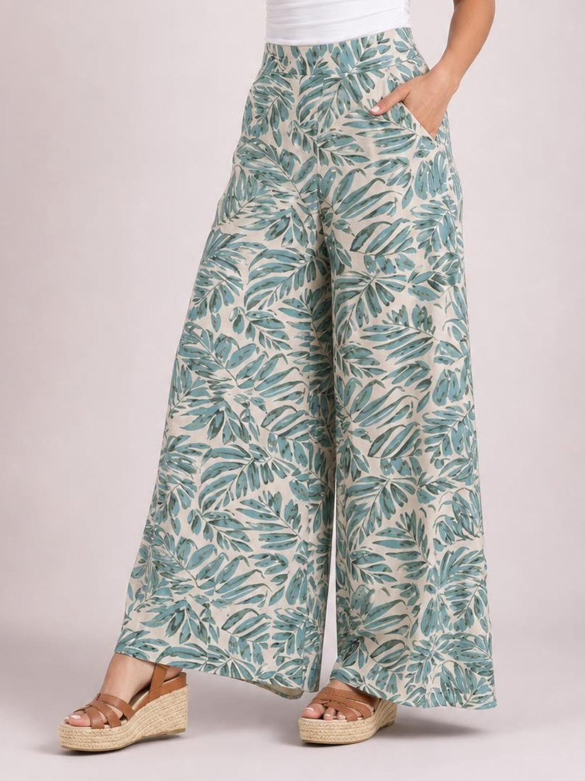 Model wearing printed high waist wide leg pants with a blue-green botanical pattern, flowing cropped silhouette, and hands in the side pockets.