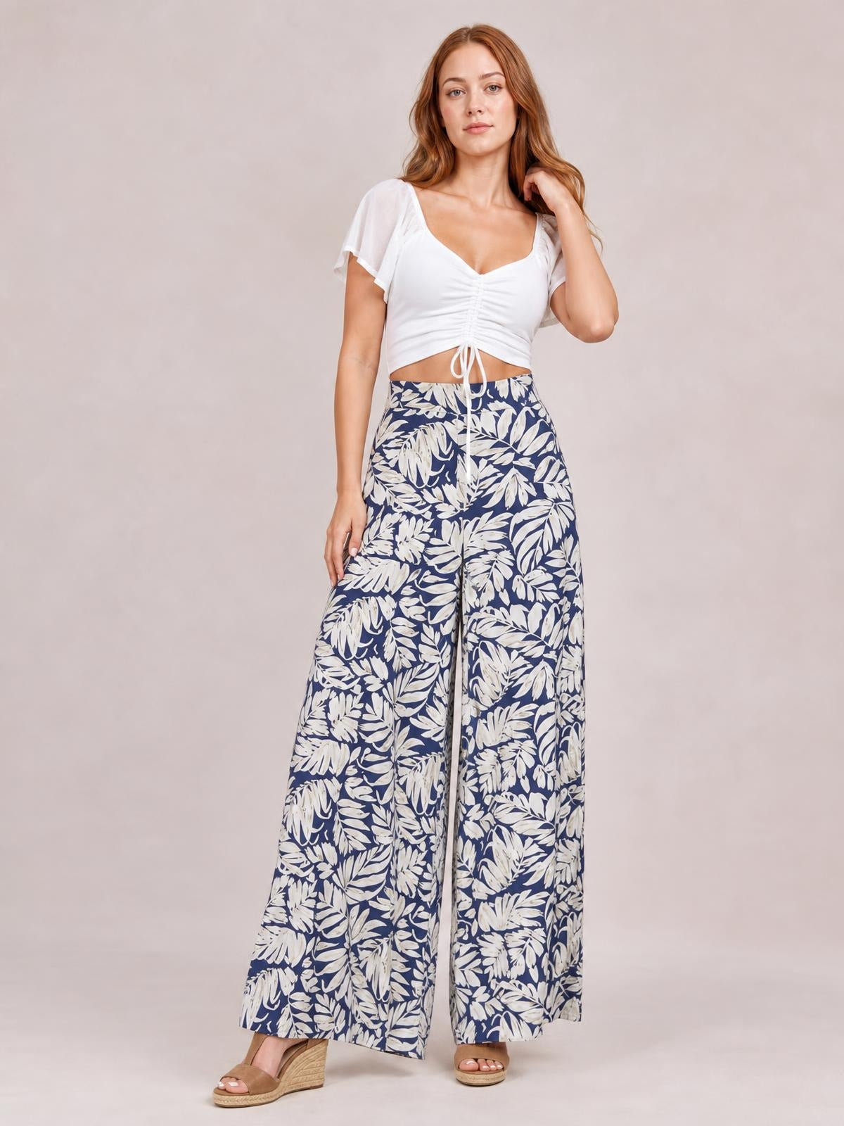 Model poses in navy and white printed high waist wide leg pants with a flowing silhouette, front drawstring waist, and full-length legs.