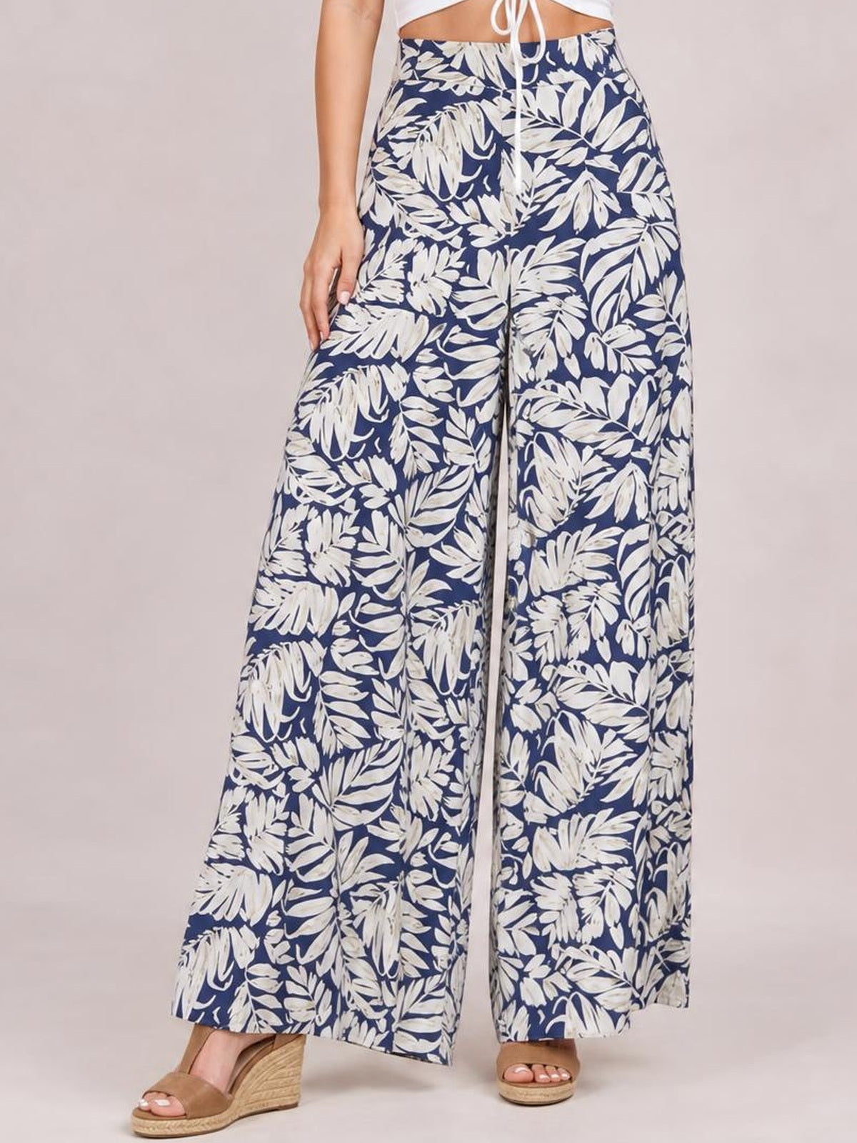 Model poses in navy and white printed high waist wide leg pants with a flowing full-length silhouette and straight waistband.