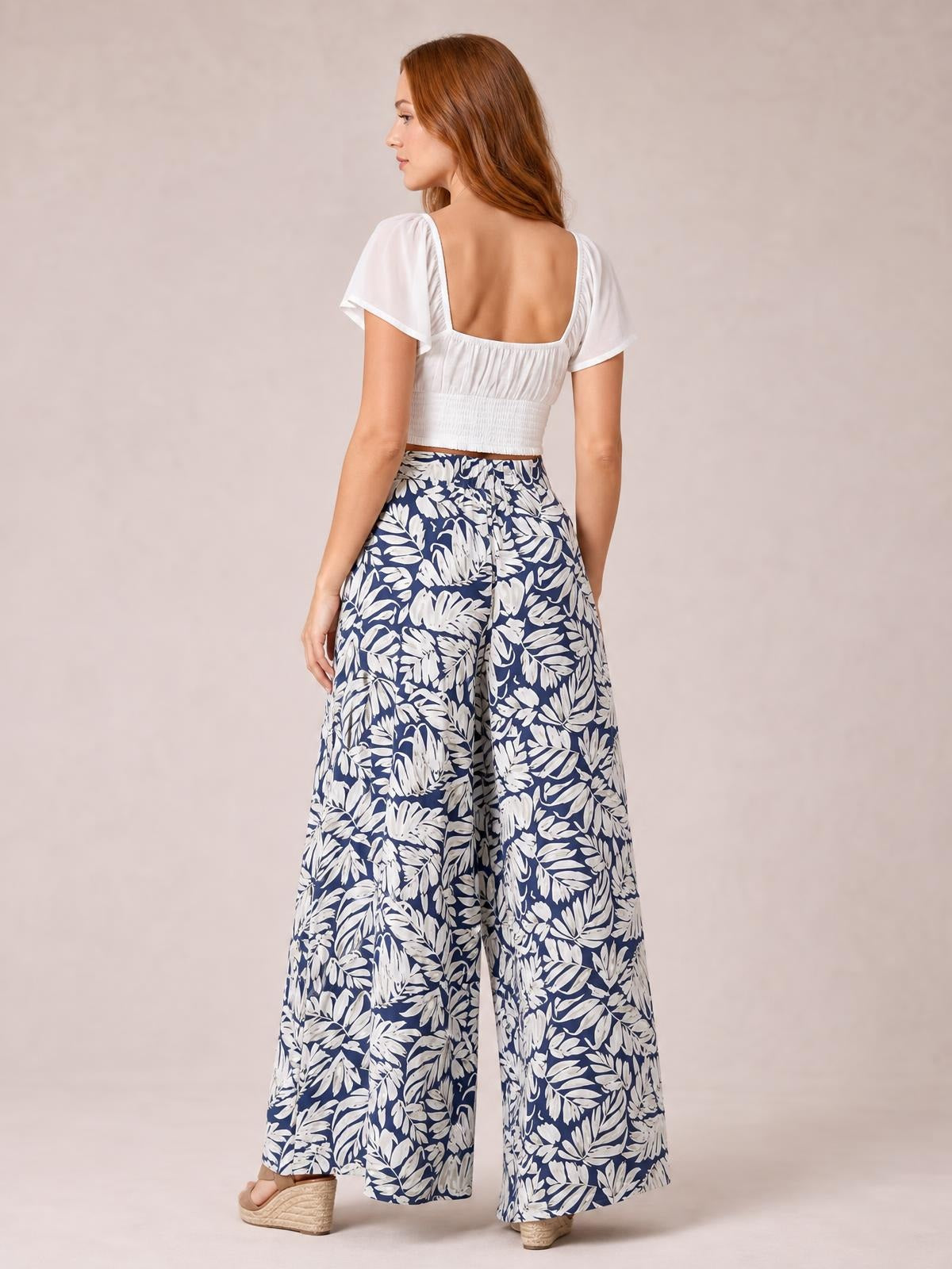 A model poses from behind in navy and white botanical-print high waist wide leg pants with a flowing, floor-length silhouette.